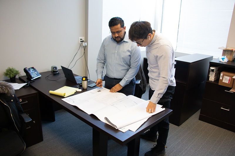 Two men are standing at a desk looking at a blueprint.