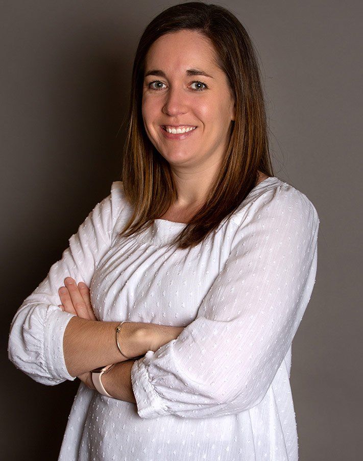 A woman in a white shirt is standing with her arms crossed and smiling.