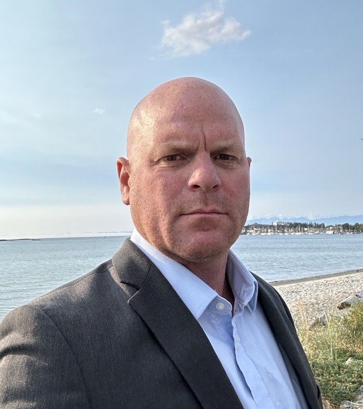 A man in a suit and white shirt is standing in front of the ocean.
