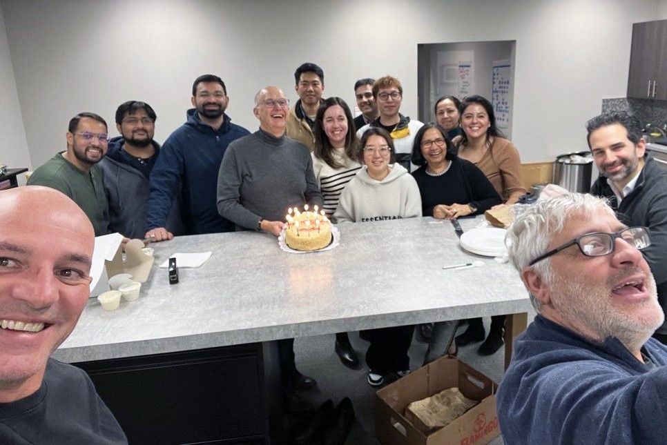 A group of people are standing around a table with a cake and candles.