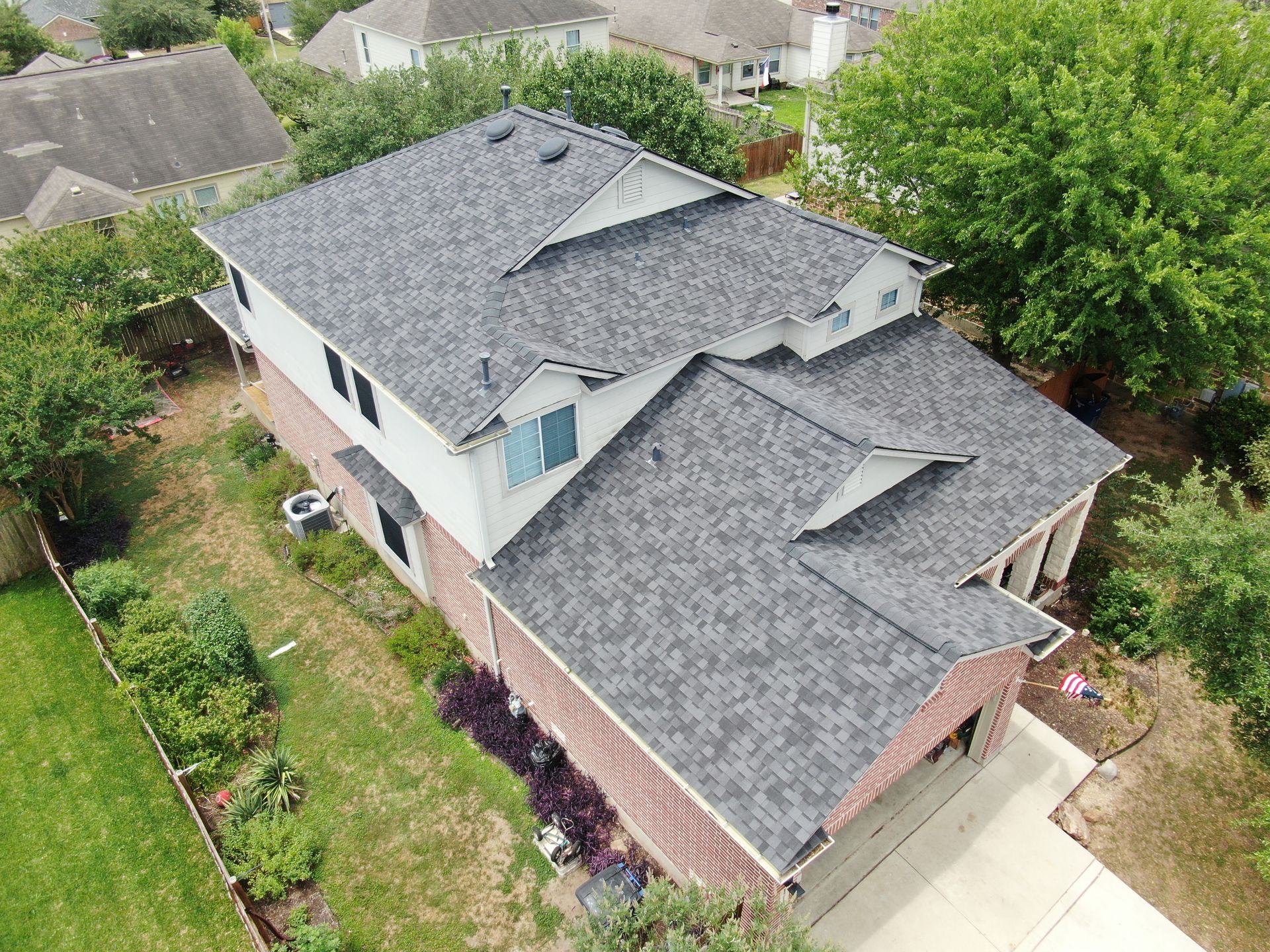 An aerial view of a house with a gray roof surrounded by trees.