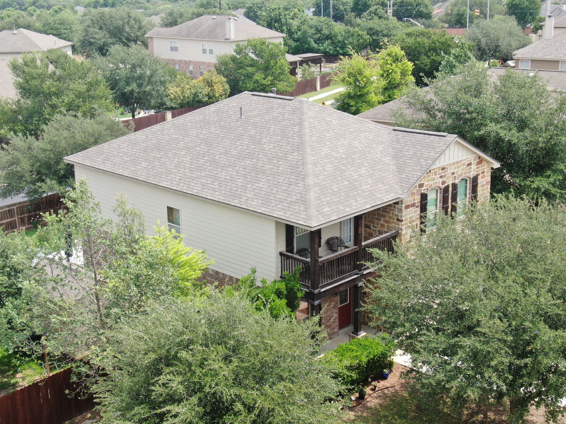 An aerial view of a house in a residential area surrounded by trees.