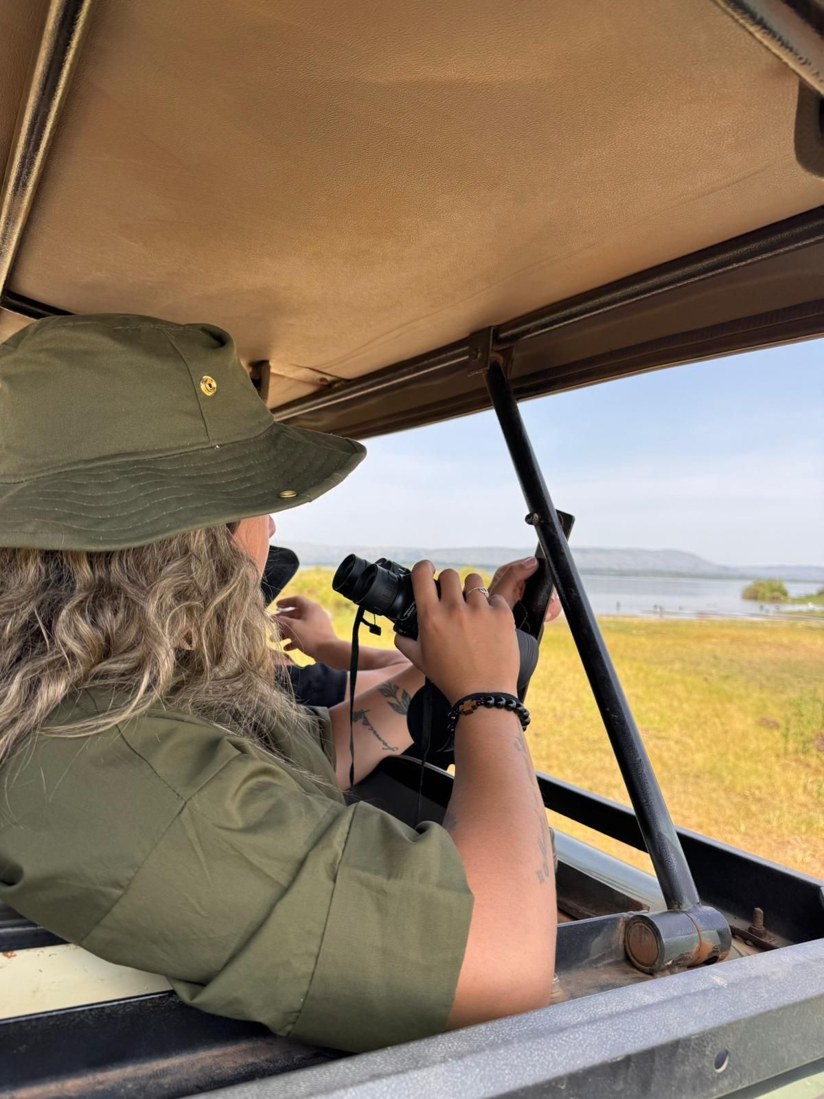 Tourist spotting animal through safari roof, holding binoculars but not using them
