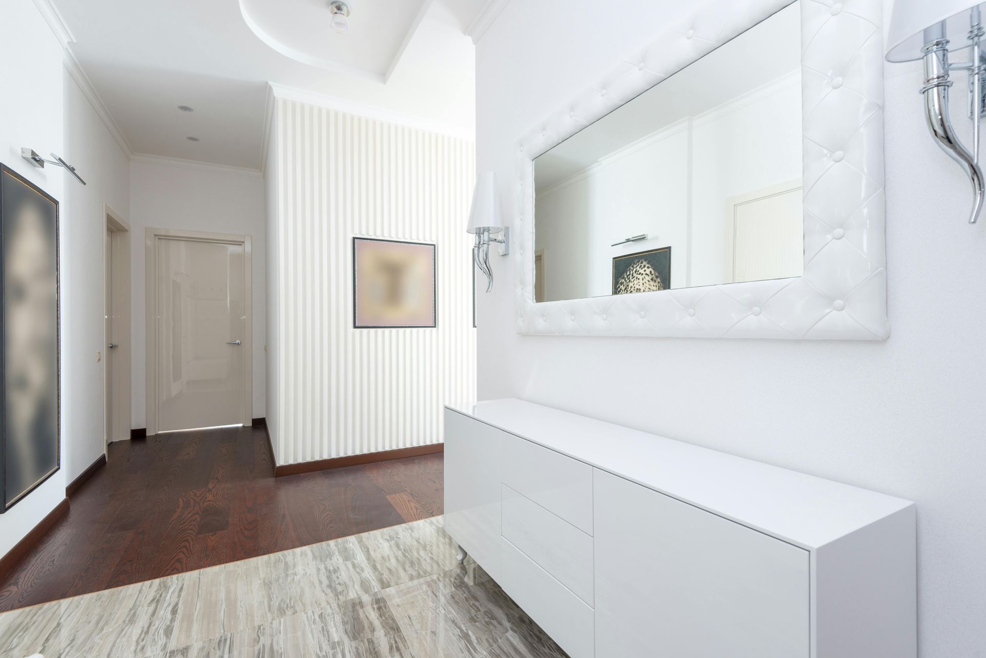 A modern, bright entryway with a white console table, a large tufted mirror, a framed print, and dark wood flooring.