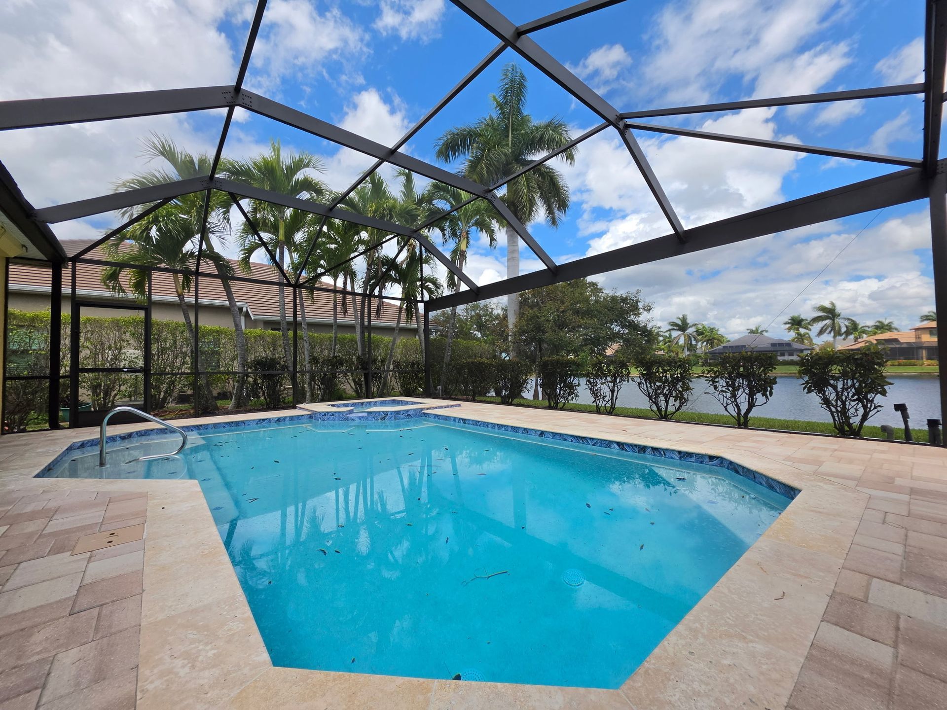 Screened-in patio with a blue swimming pool, palm trees, and water view under a partly cloudy sky
