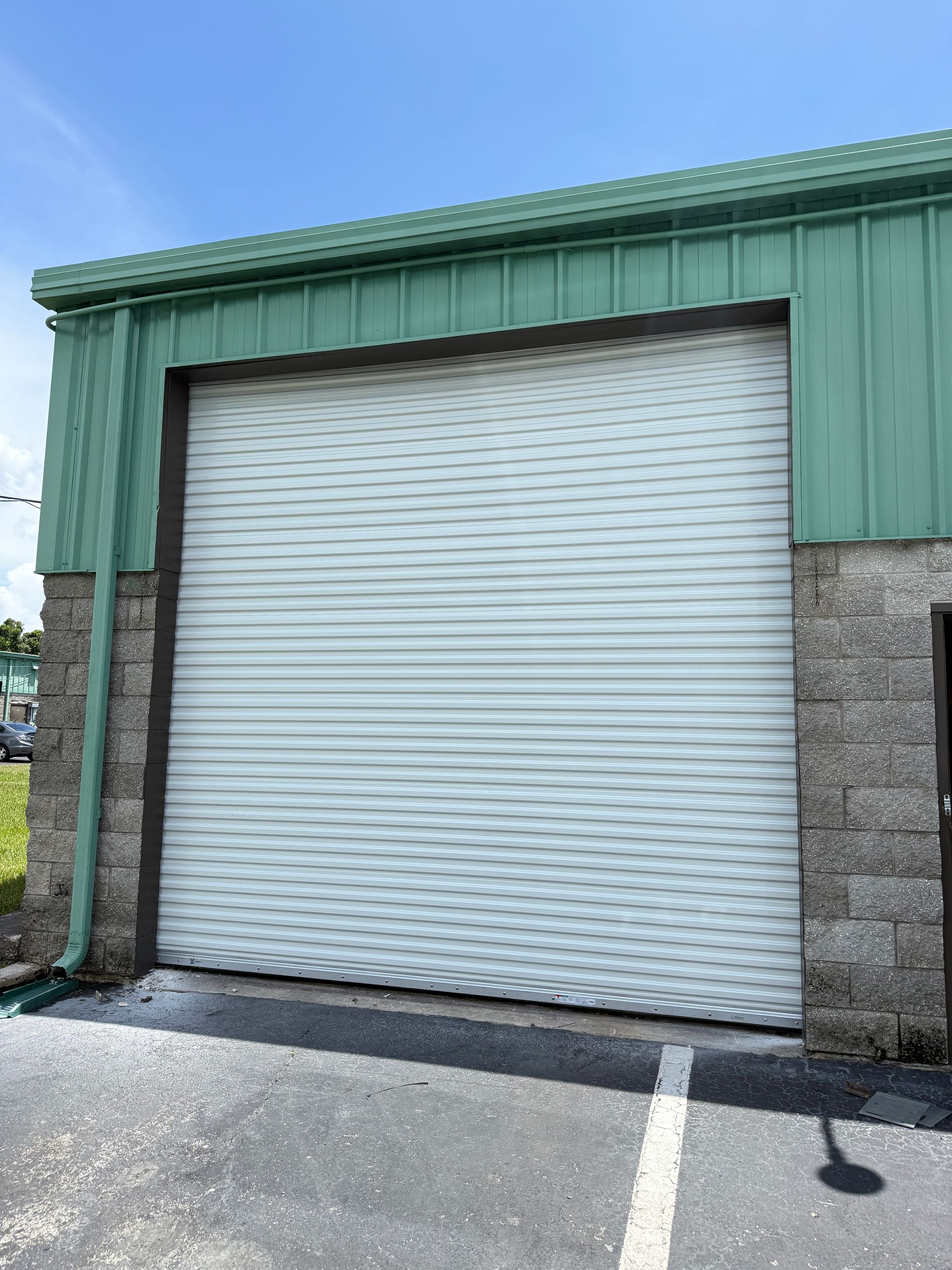 Closed white roll-up door on a green industrial building with stone lower walls.