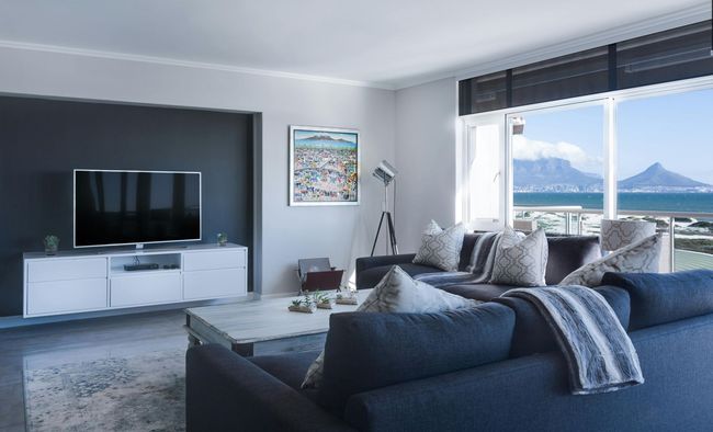 Bright modern living room with gray sofa, TV, and large windows overlooking mountains and water