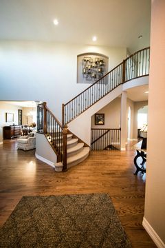 Bright foyer with curved staircase, hardwood floors, and white walls in a large home.