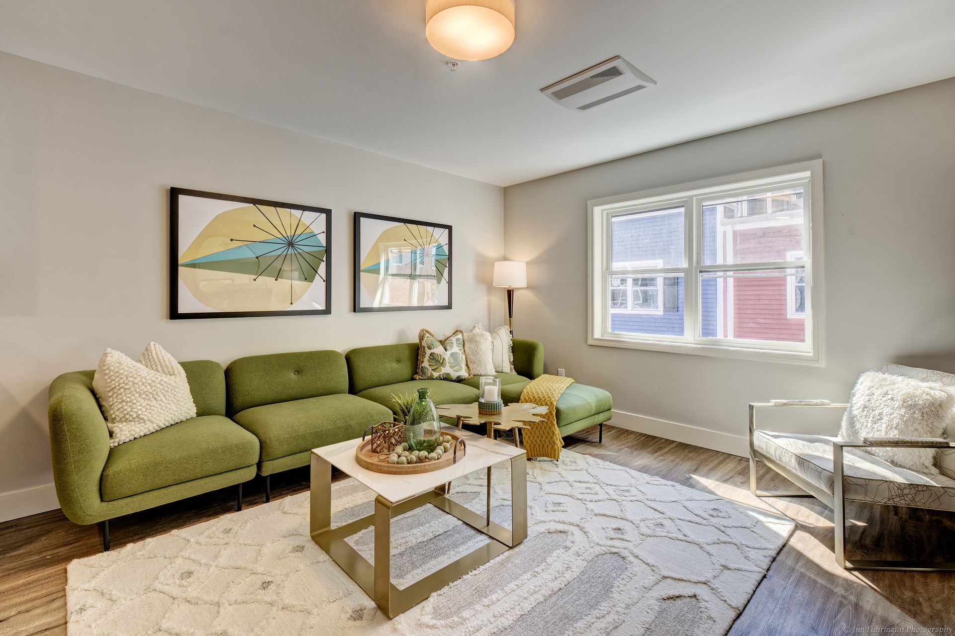 Green sectional sofa in a living room with artwork, a white rug, and a modern armchair.