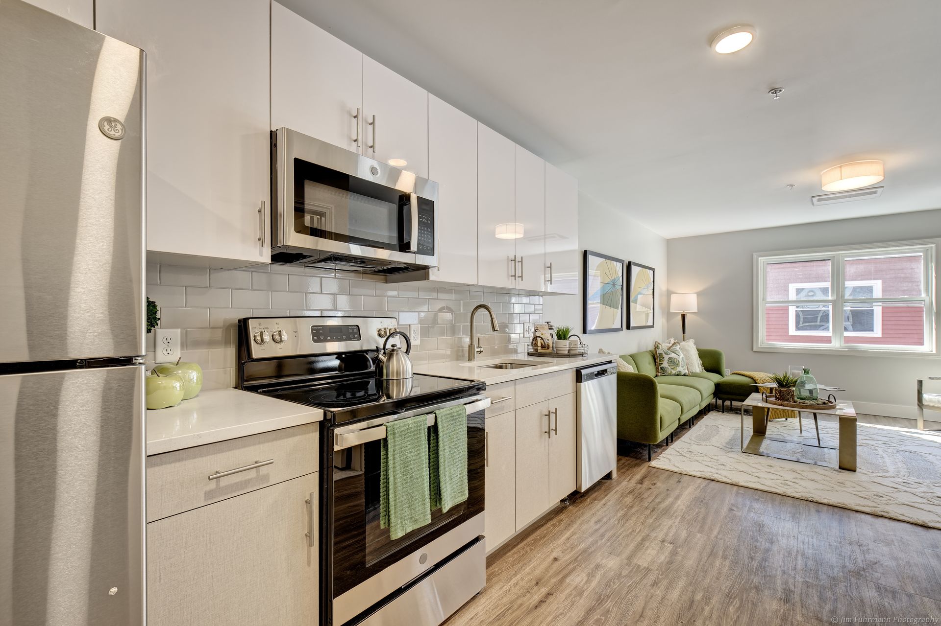 Modern kitchen with white cabinets, stainless steel appliances, and a green couch in the living area.