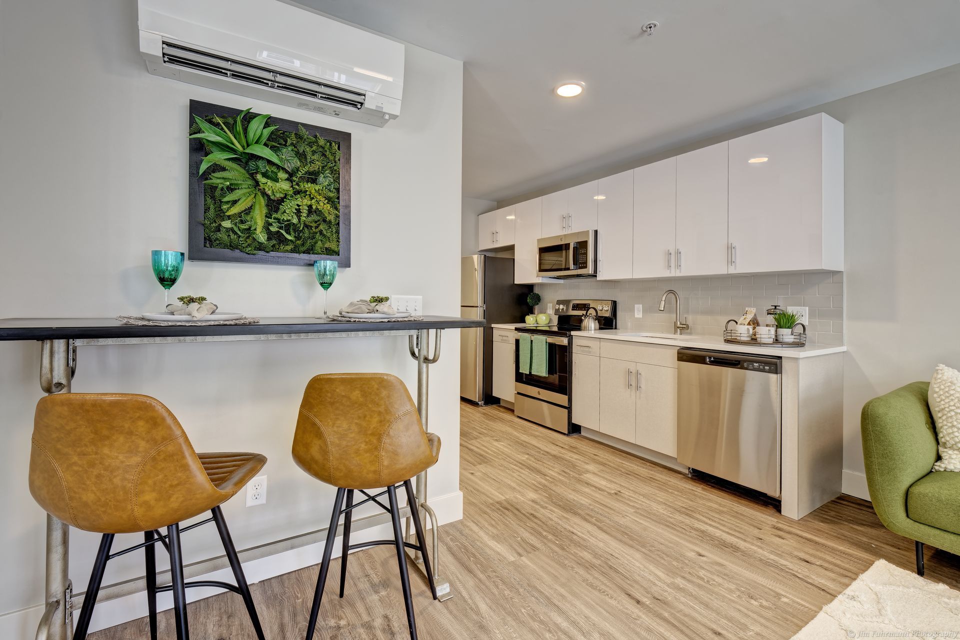 Modern apartment kitchen with stainless steel appliances, white cabinets, and a breakfast bar with two brown stools.