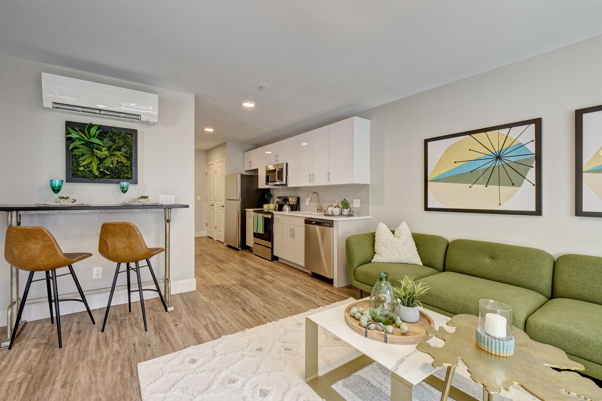 A living room with a green couch , coffee table , stools and a kitchen.