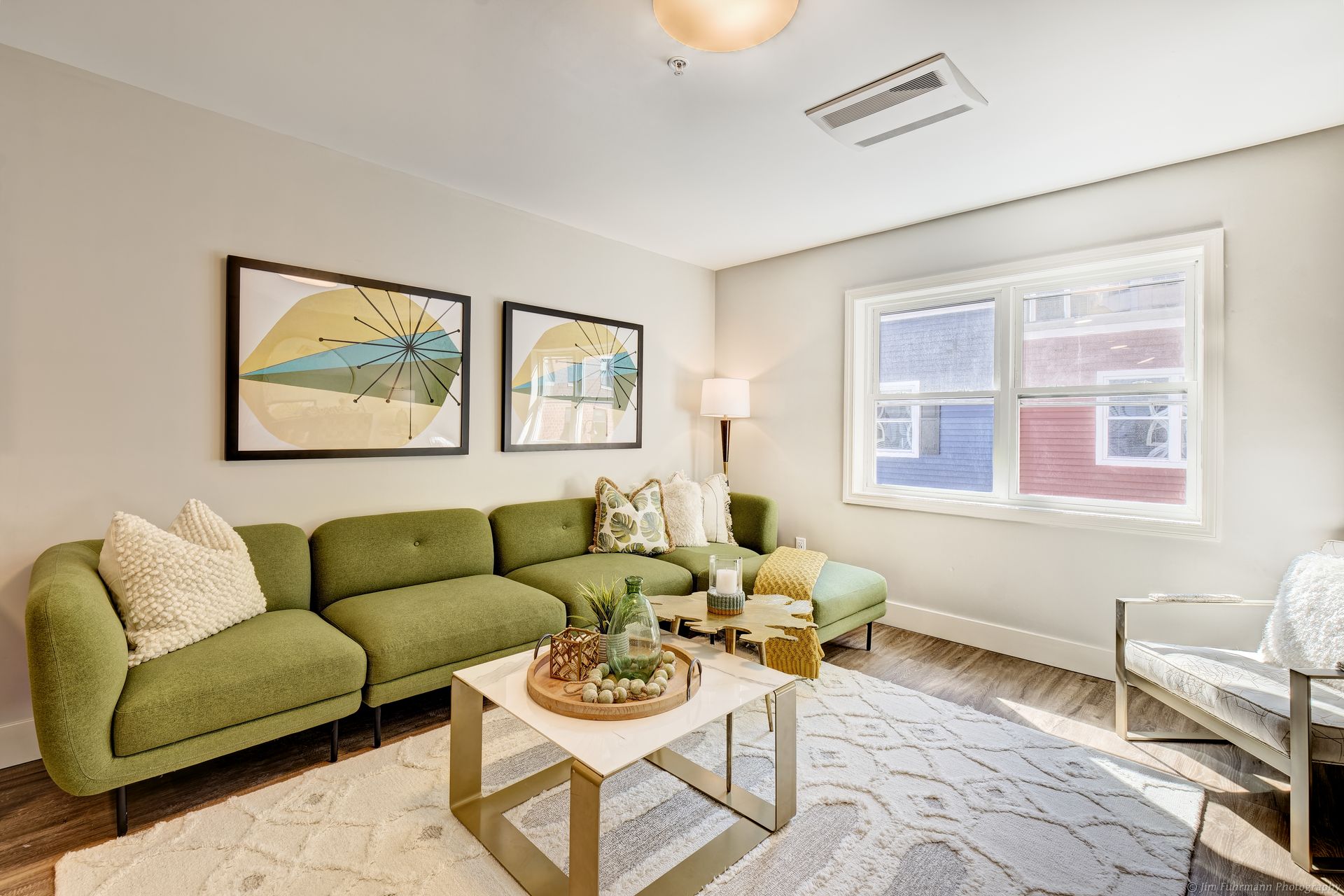 Green sectional sofa in a living room with art, a coffee table, and a window looking out to red building.