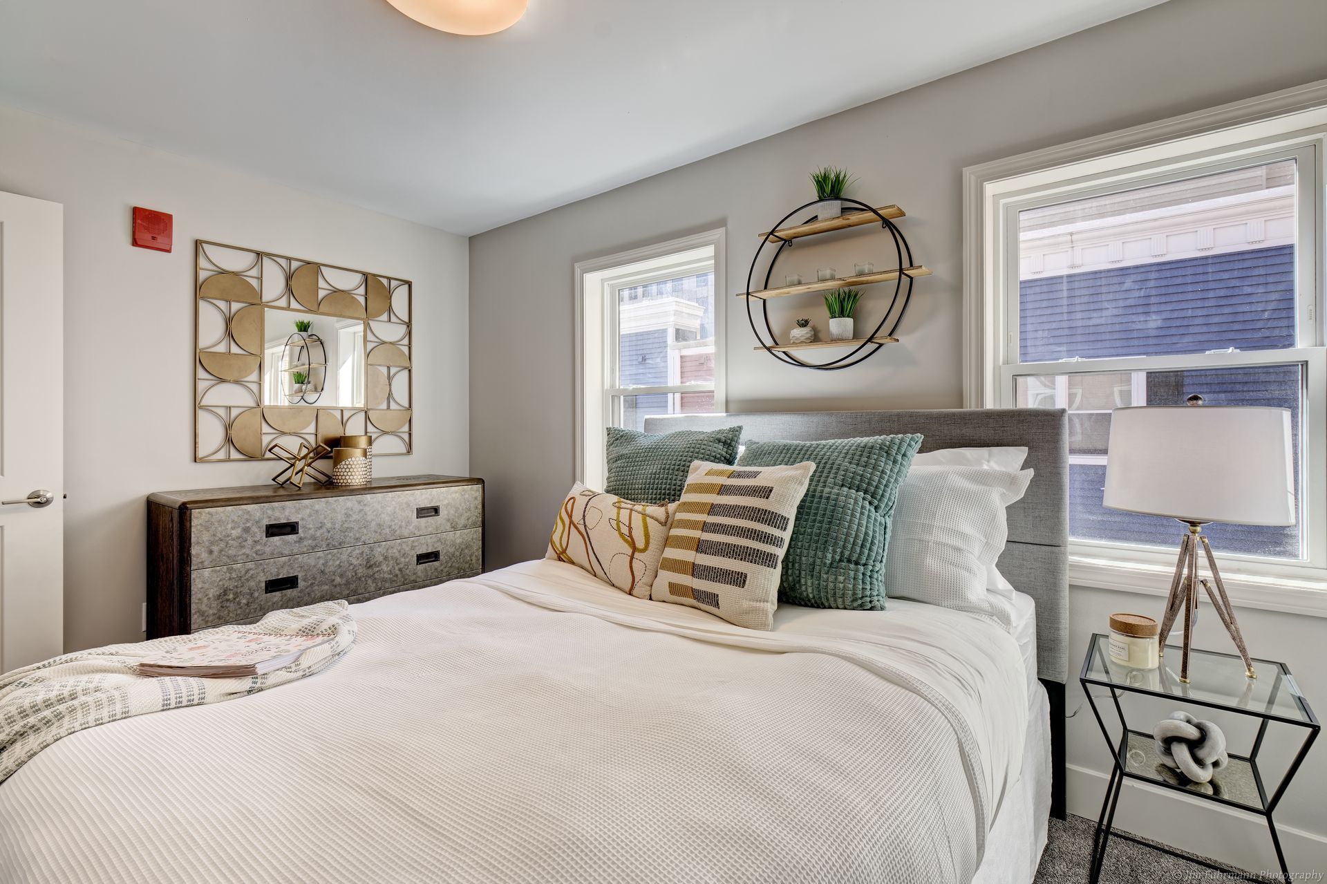 Cozy bedroom with a bed, nightstand, and dresser.  Neutral color scheme, with patterned pillows and decorative mirror.
