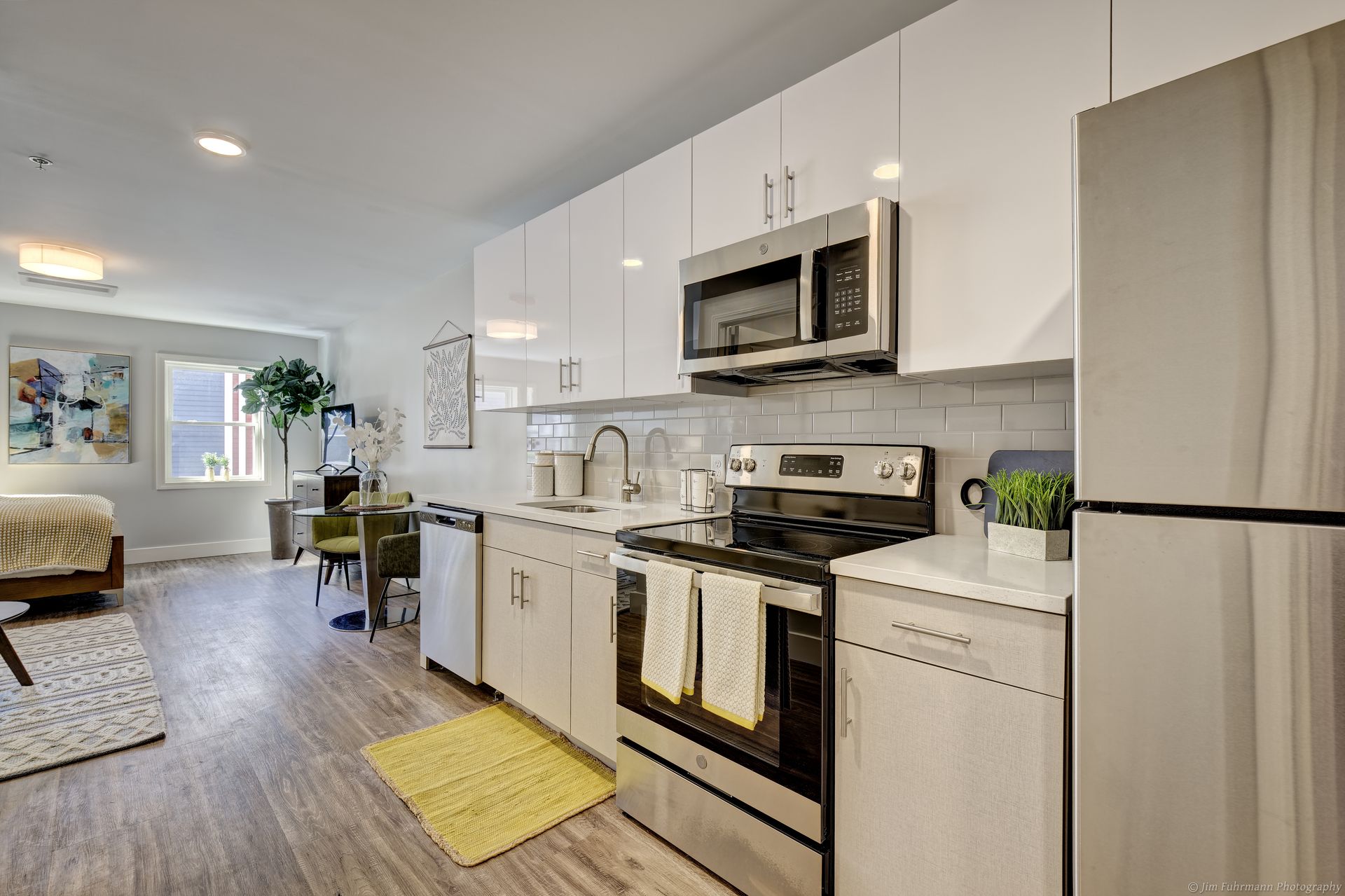 Modern kitchen with white cabinets, stainless steel appliances, and a yellow rug on a light wood floor.