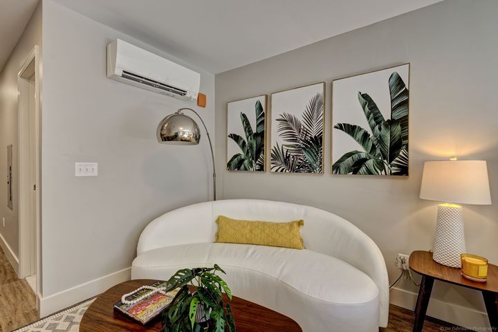 A small living room with a white curved sofa, wood side table, and three botanical art prints on a gray wall.