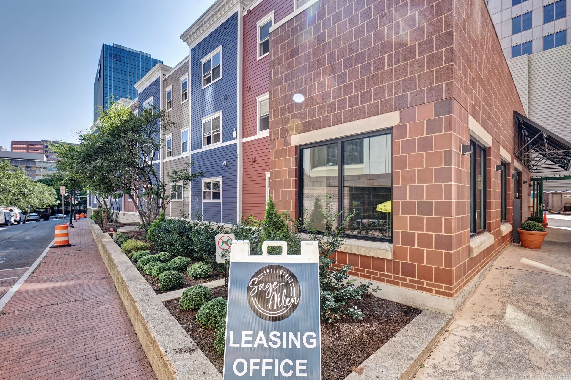 Exterior view of a leasing office with a sign, brown brick, and blue siding on a sunny day.
