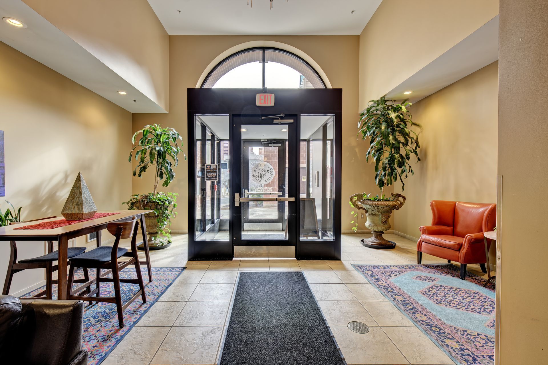 An interior entrance hall with an arched window above the doors. There is a table with chairs, plants, and a red armchair.