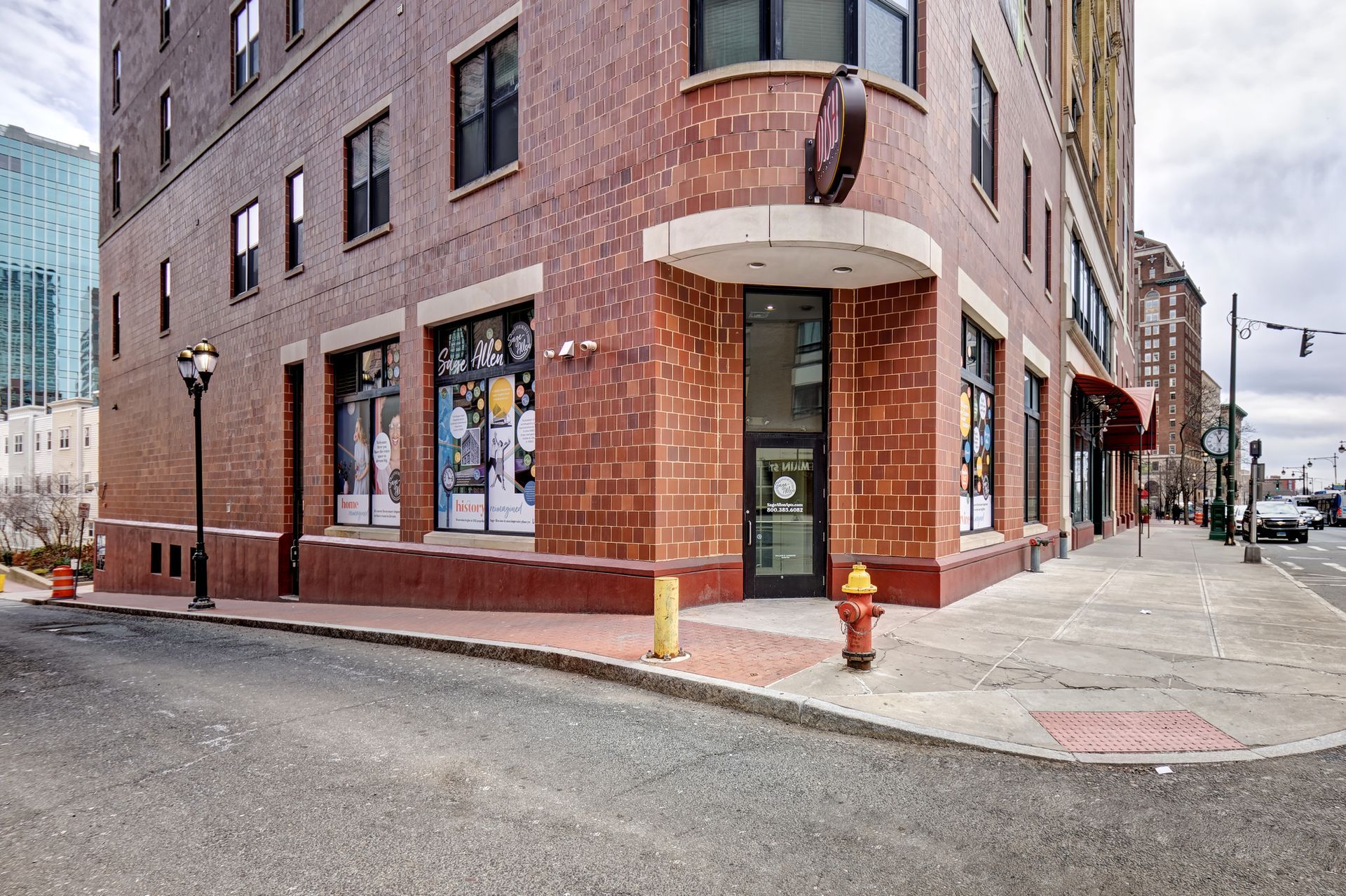 A brick building on a street corner with large windows, an arched entrance, and a red fire hydrant.