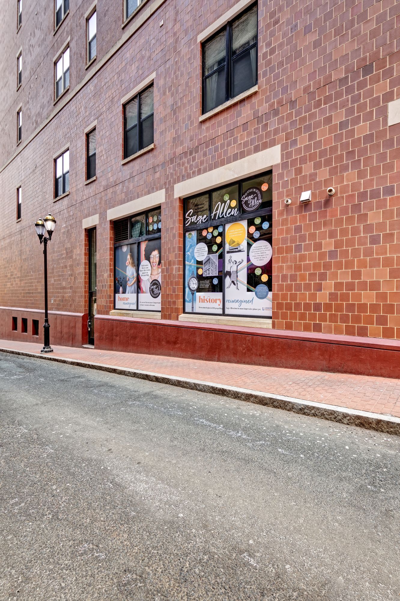An alleyway with a brick building. Two storefront windows are at street level; a black lamppost stands at left.