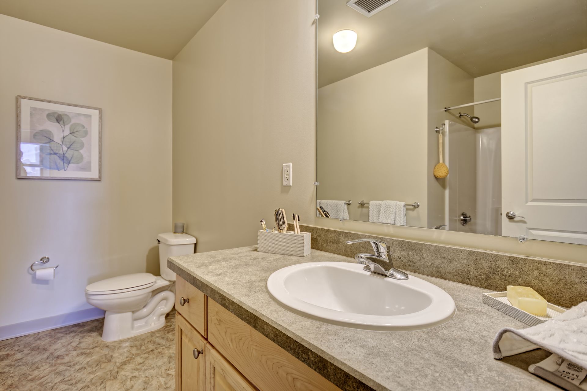 Bathroom with a sink, toilet, and shower. Beige walls, light wood cabinets, and a large mirror.