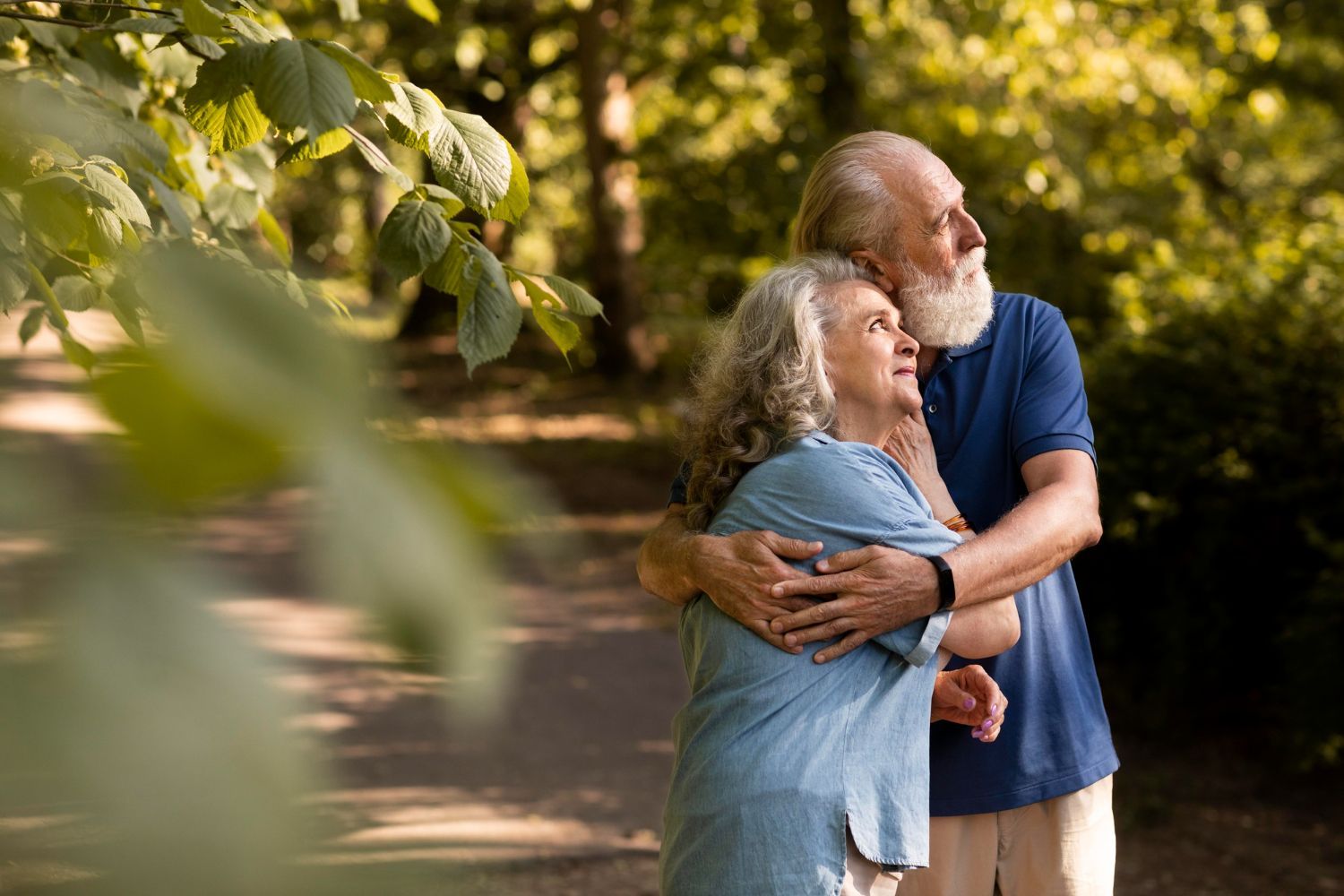 An elderly couple is hugging each other in a park.