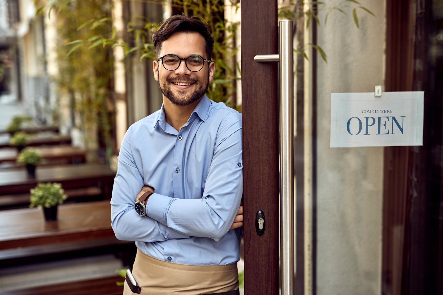 A man is standing in front of a restaurant door with his arms crossed.