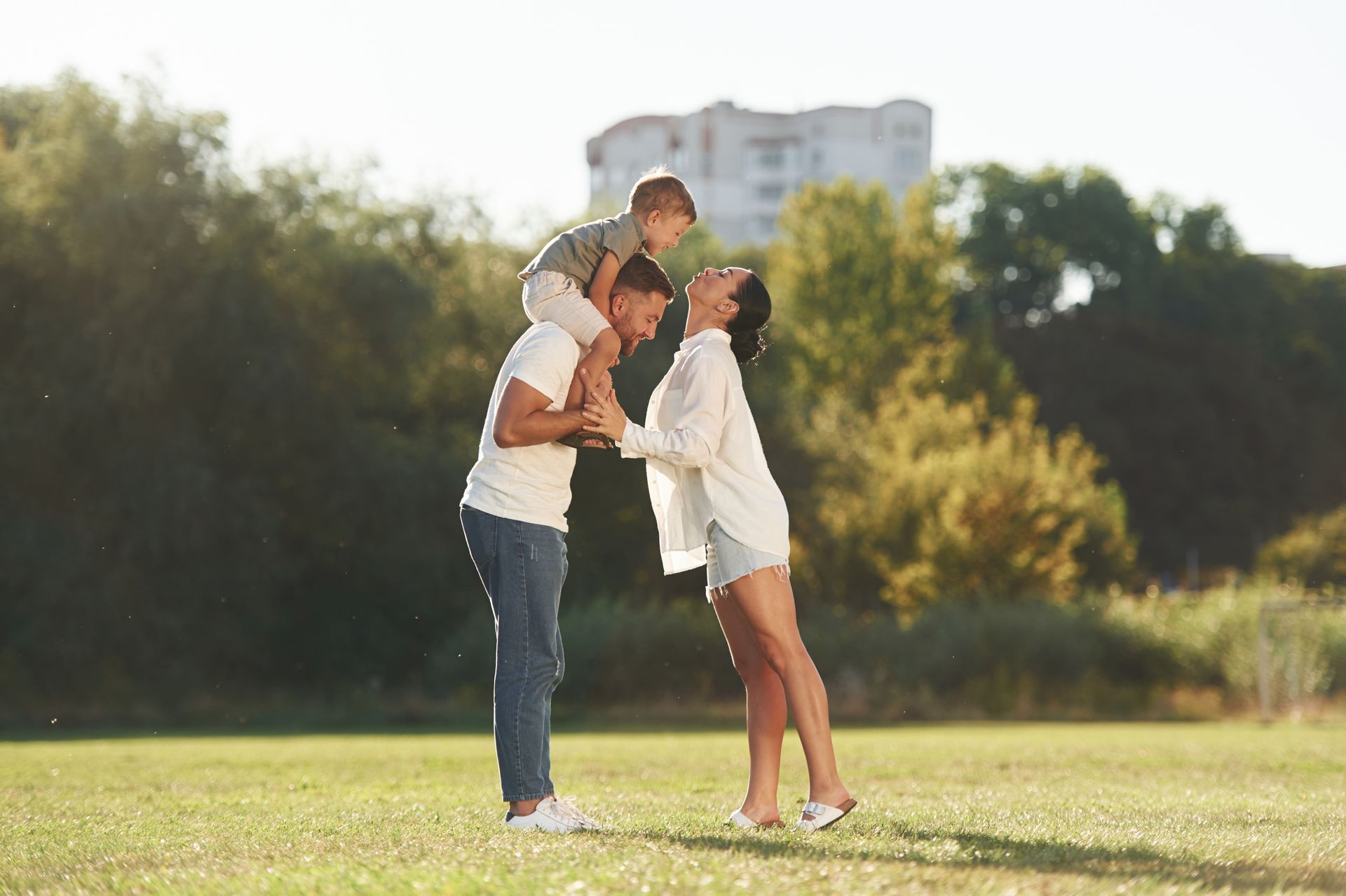 A man is carrying a child on his shoulders in a park.