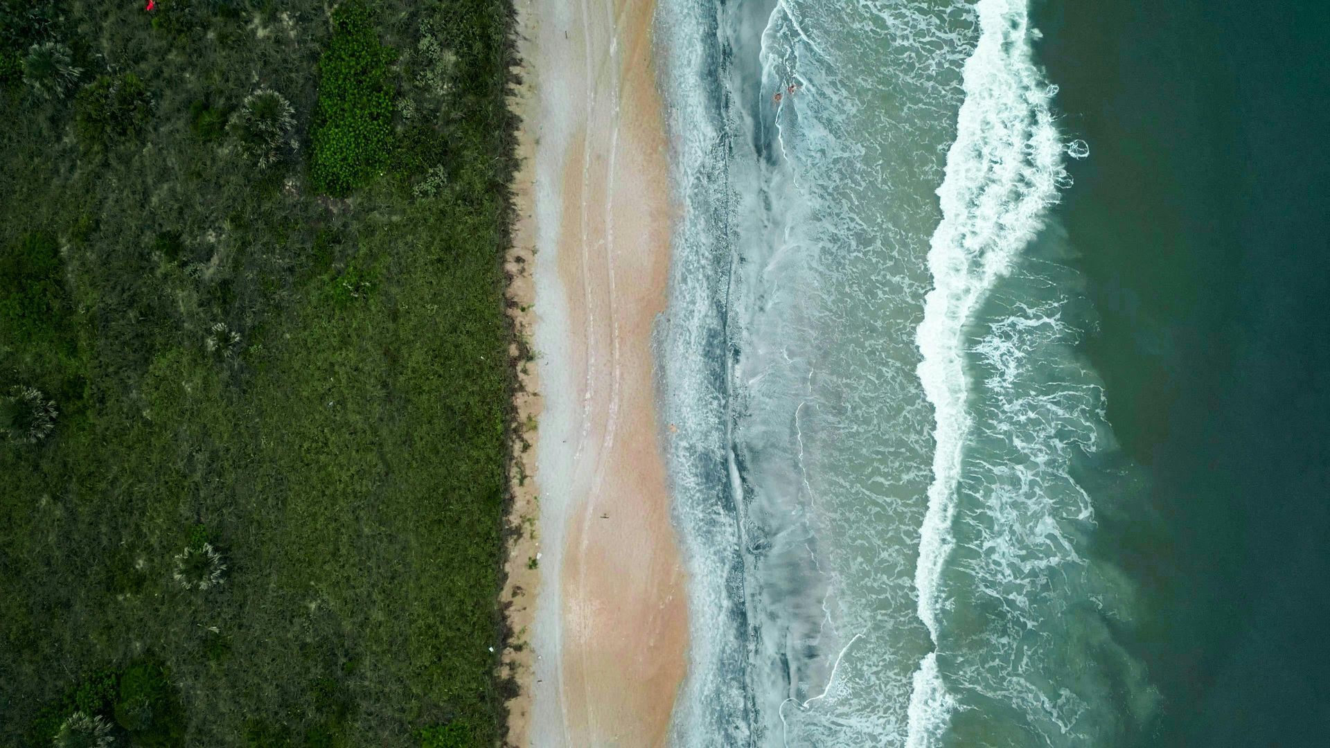 An aerial view of a beach with waves crashing on the shore.