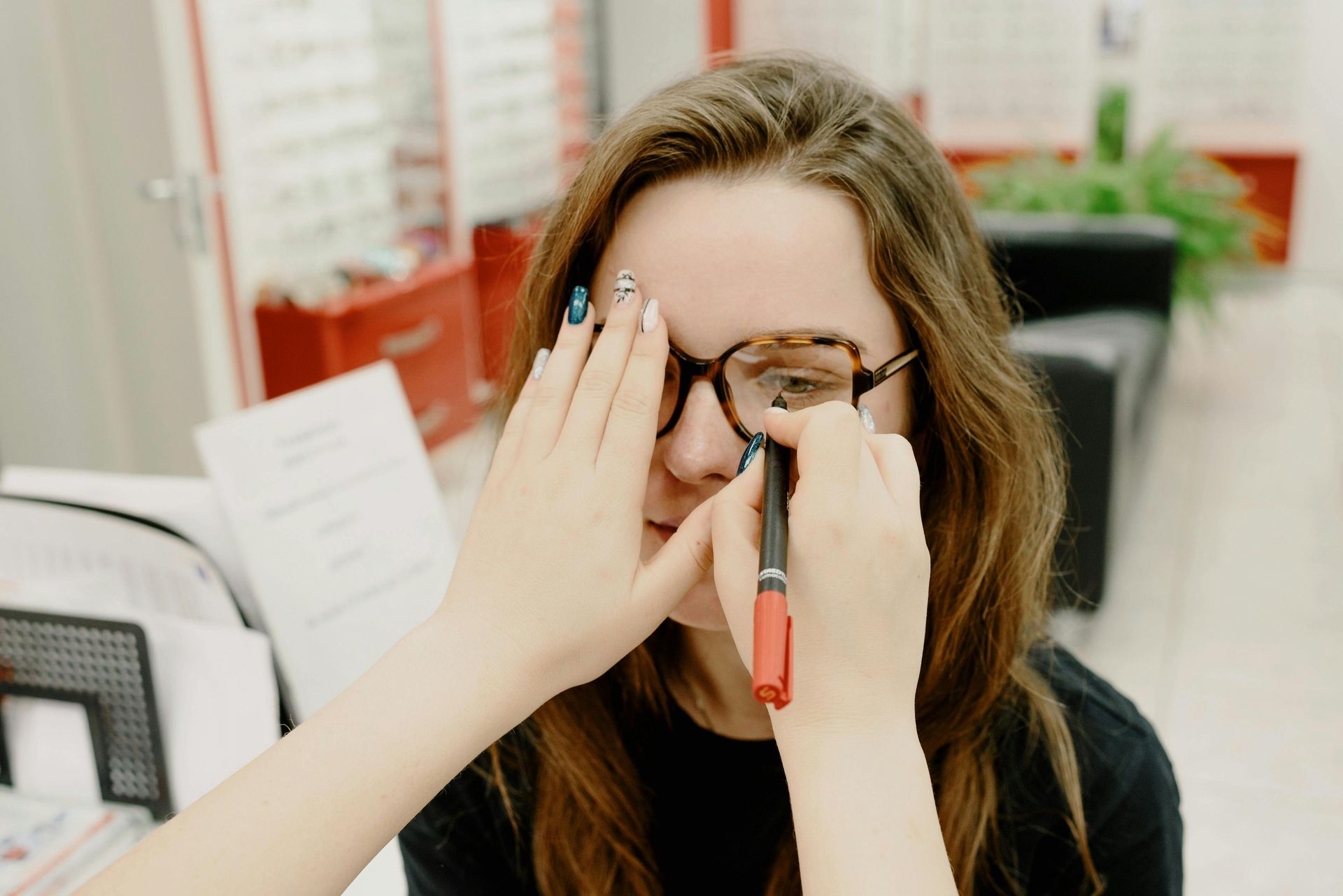 A woman has an eye exam. A person holds a pen in front of her eye while she covers the other. Inside an optometry office.
