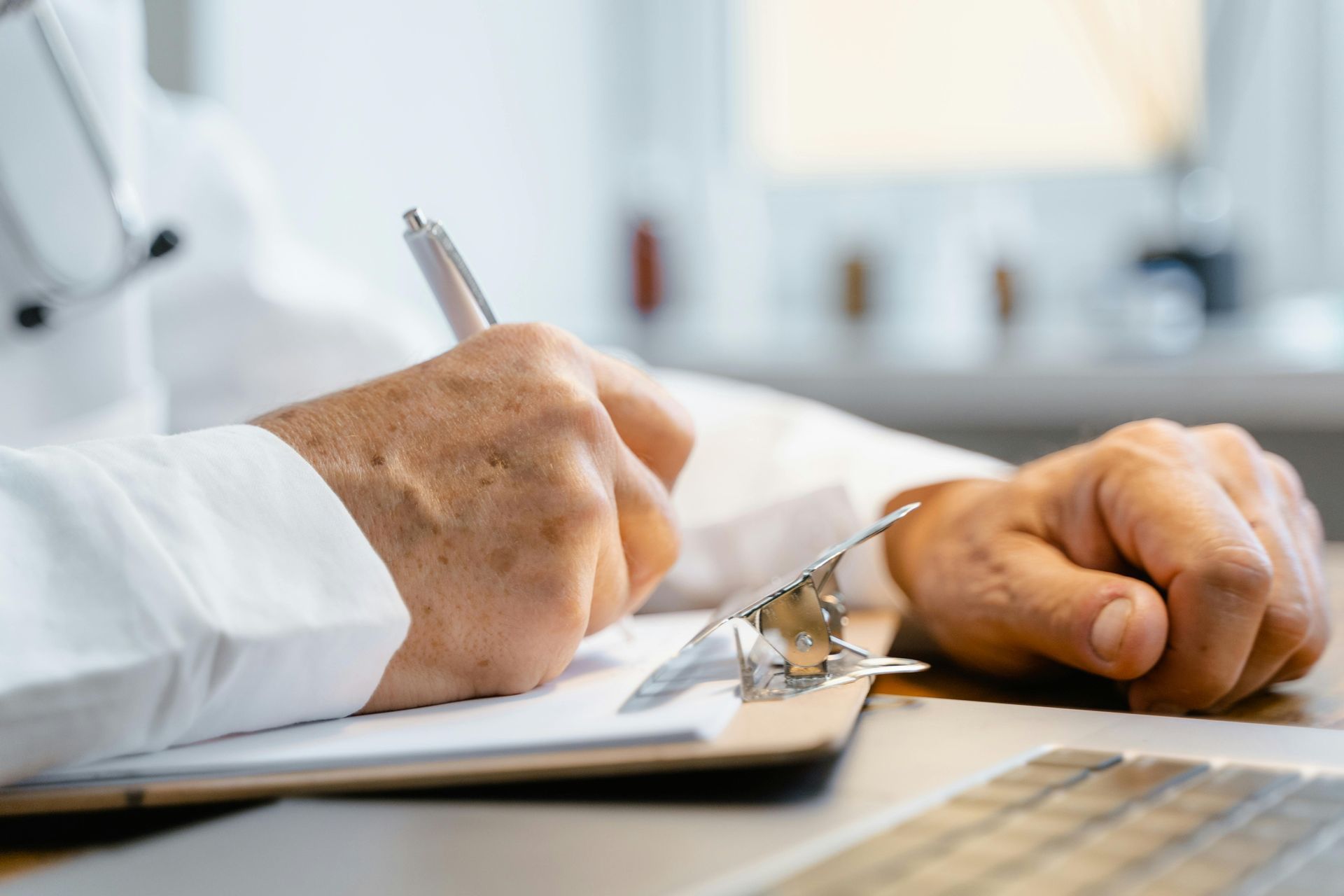 A doctor is writing on a clipboard with a pen.