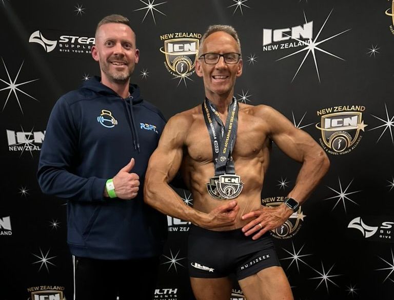 Ray and client Ken are posing for a picture in front of a banner that says icn new zealand