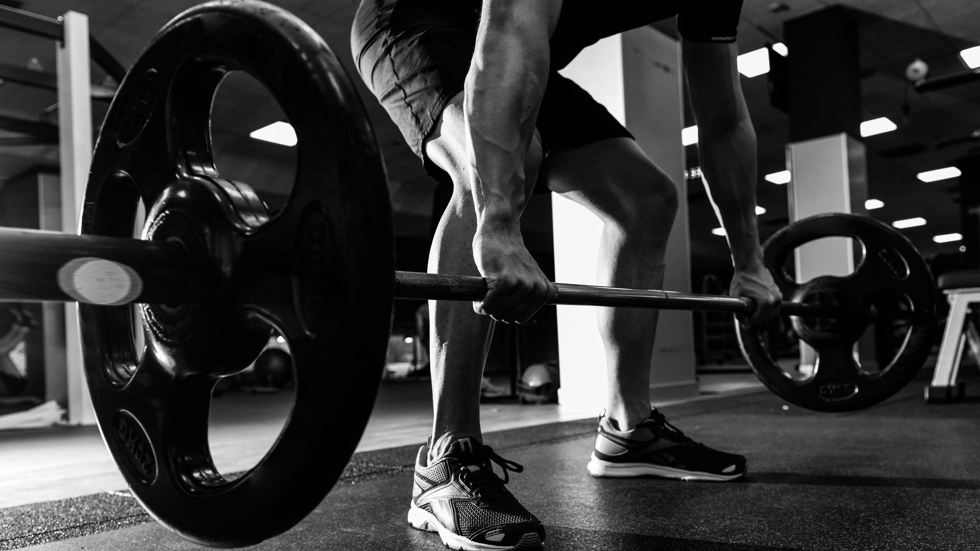 A man is lifting a barbell in a gym in a black and white photo.