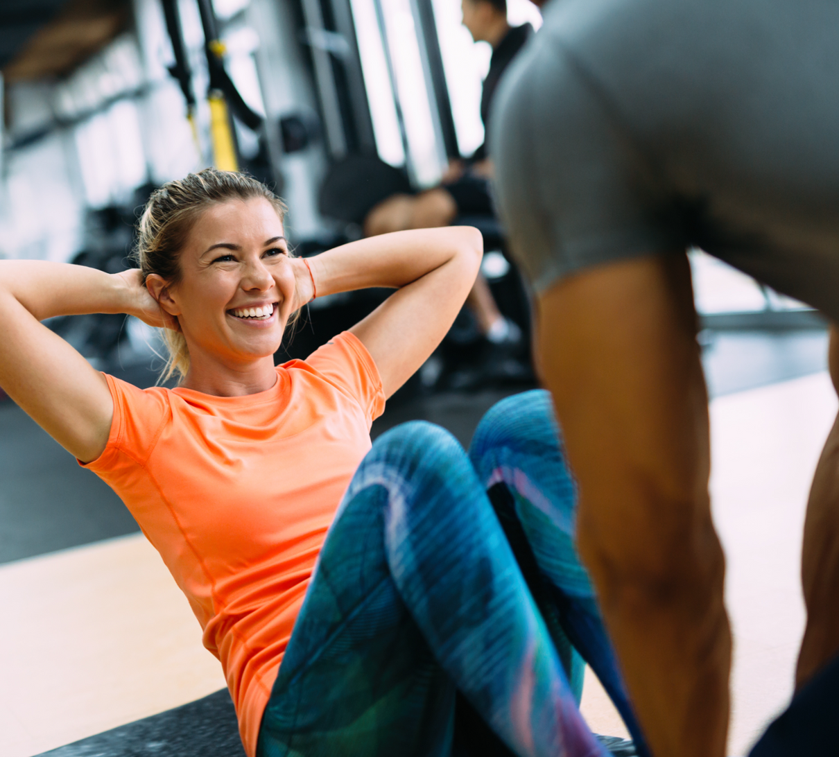 A personal trainer helping a woman do sit ups in a gym.