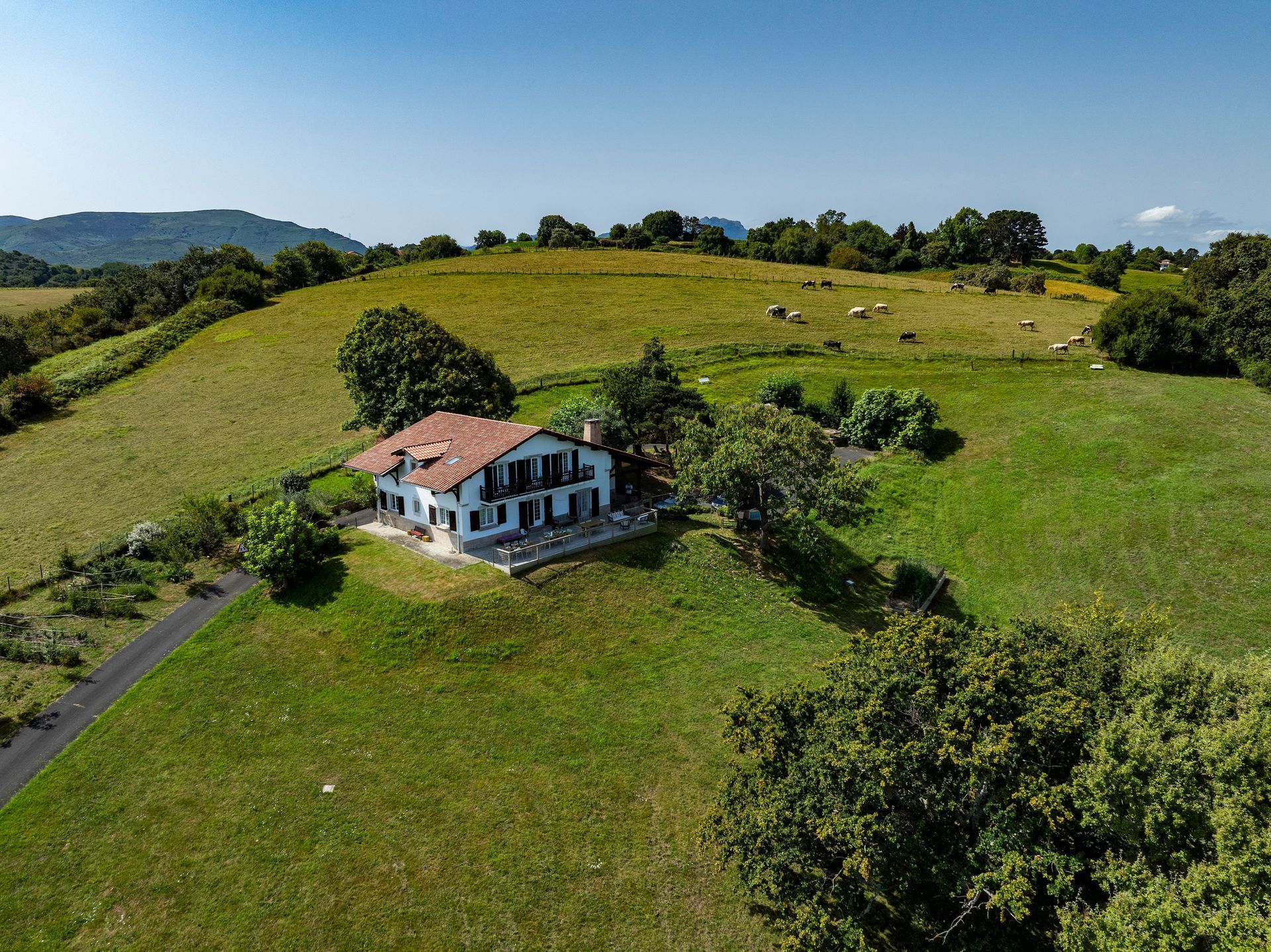 White house with red roof in a grassy field with trees under a blue sky.