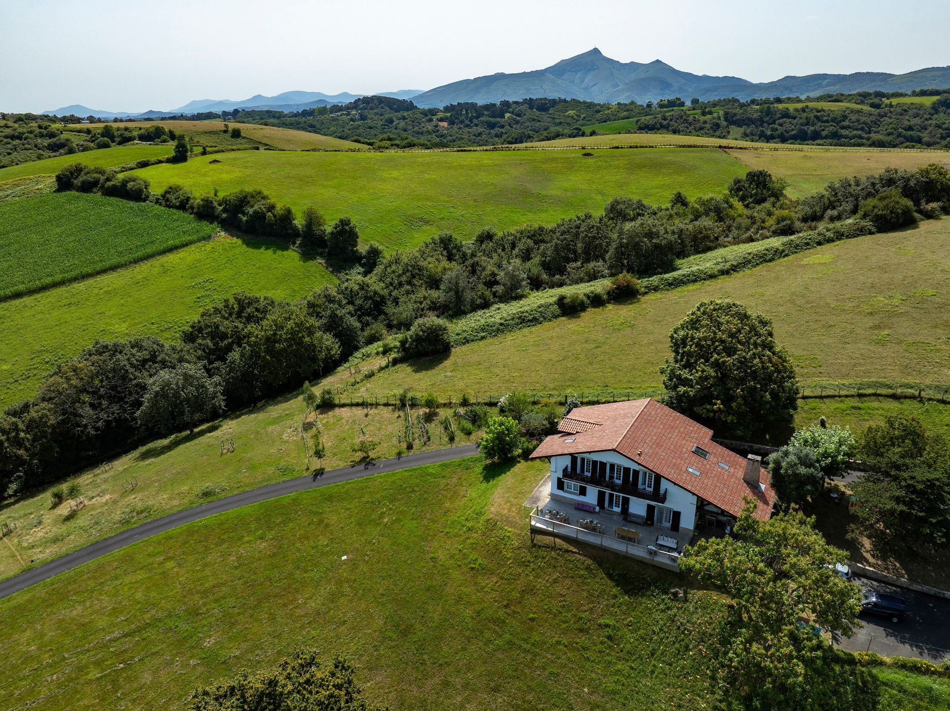 A house with a red roof in a green, hilly landscape. Distant mountains. Sunny day.