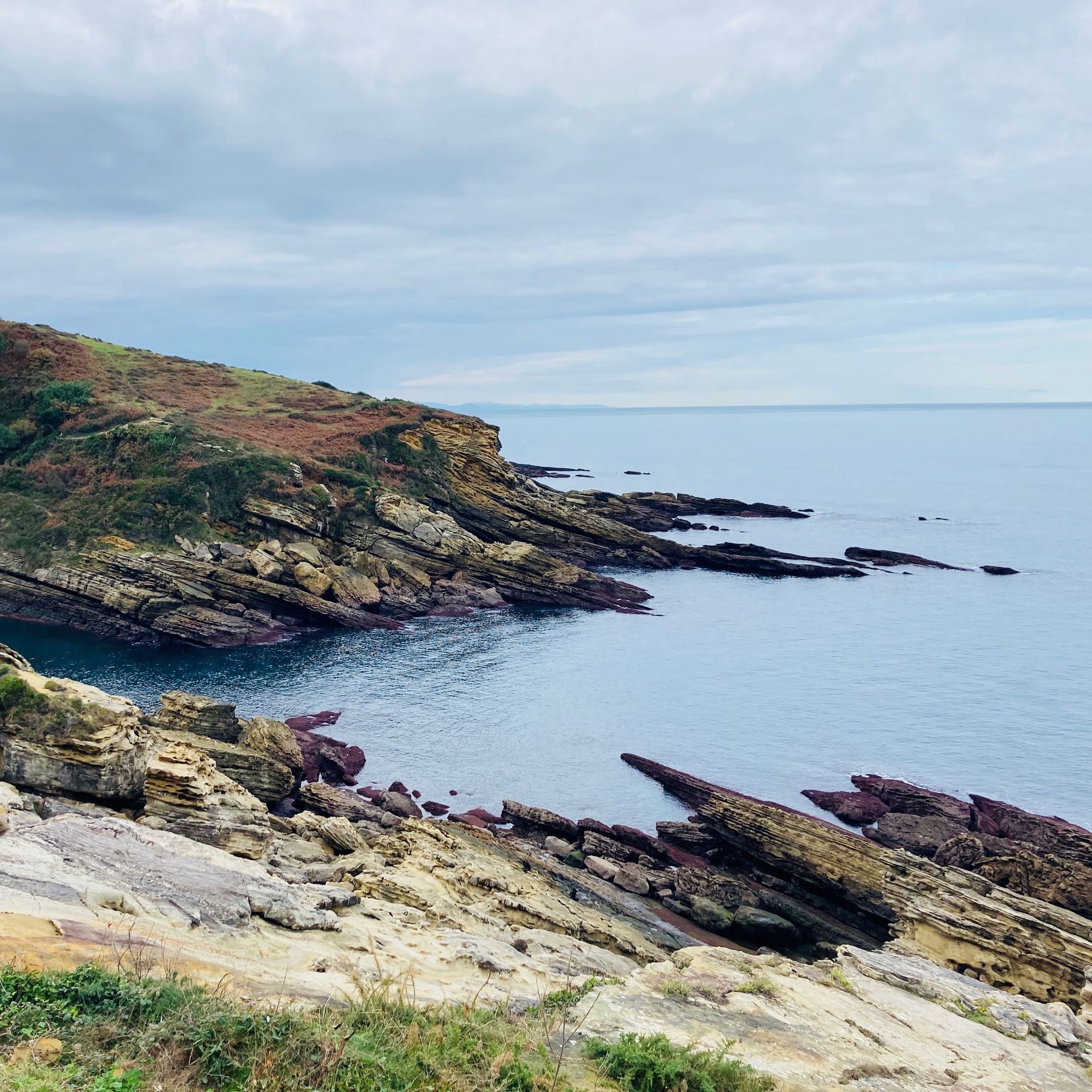 Rocky coastline with blue ocean under a cloudy sky.