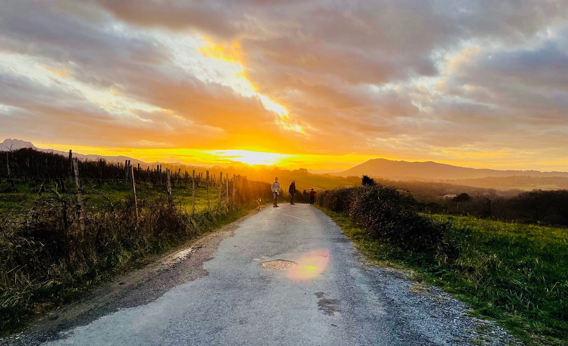 A sunset over a path, with a bright yellow sun, clouds, and distant hills.