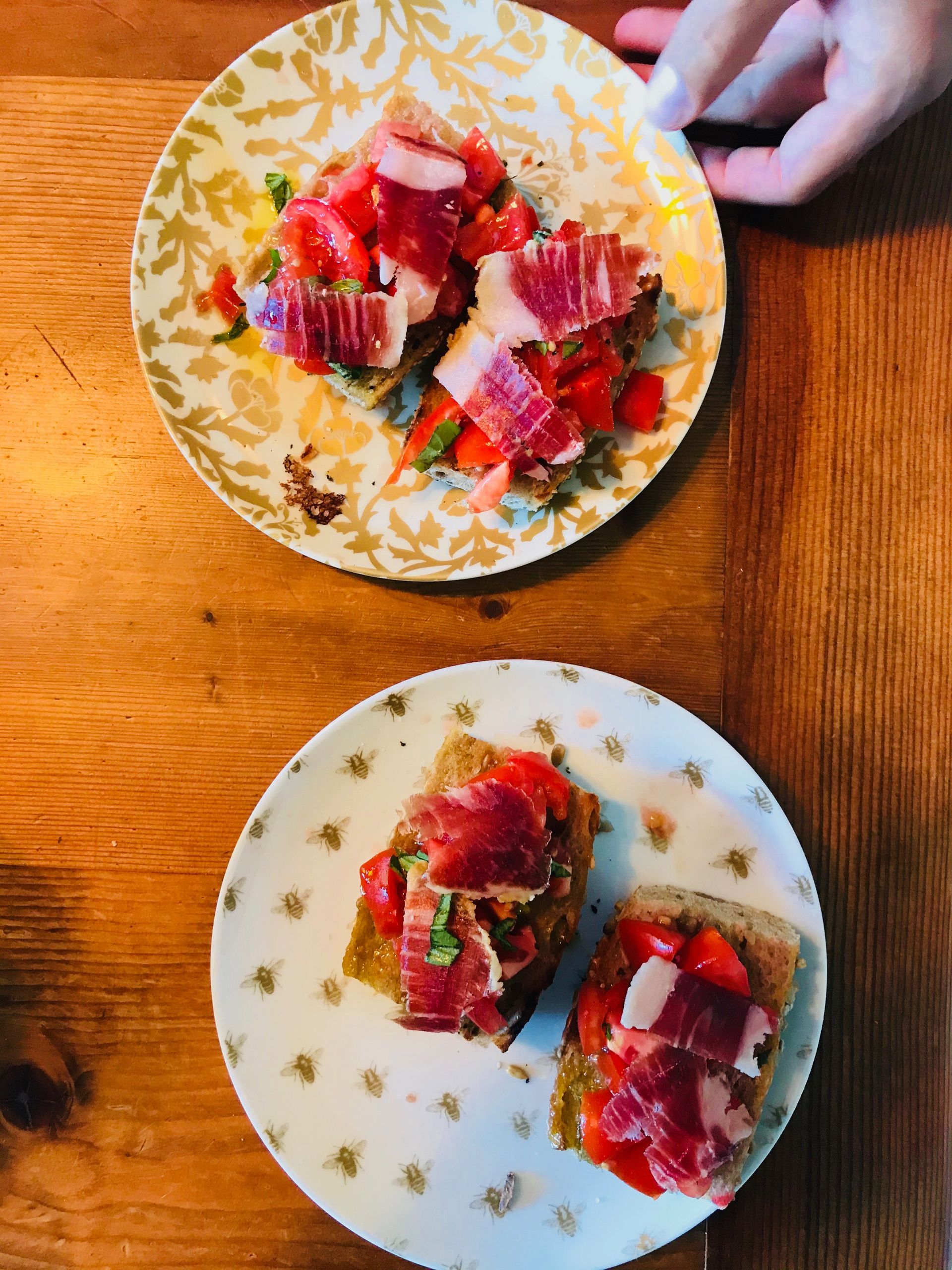Two plates of bruschetta topped with tomatoes and prosciutto on a wooden table.