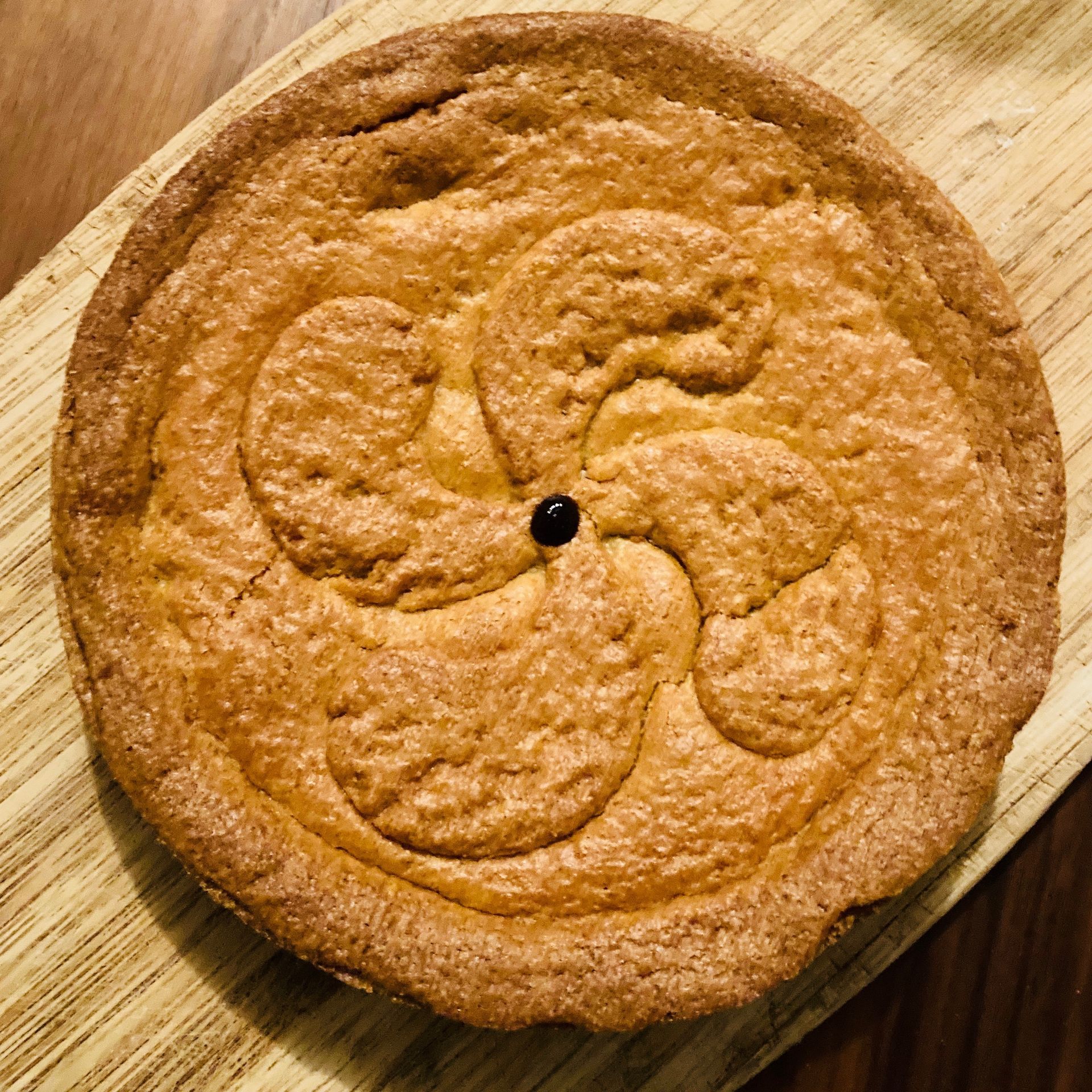 Round, golden-brown pie with a decorative, swirling design in the center on a wooden board.