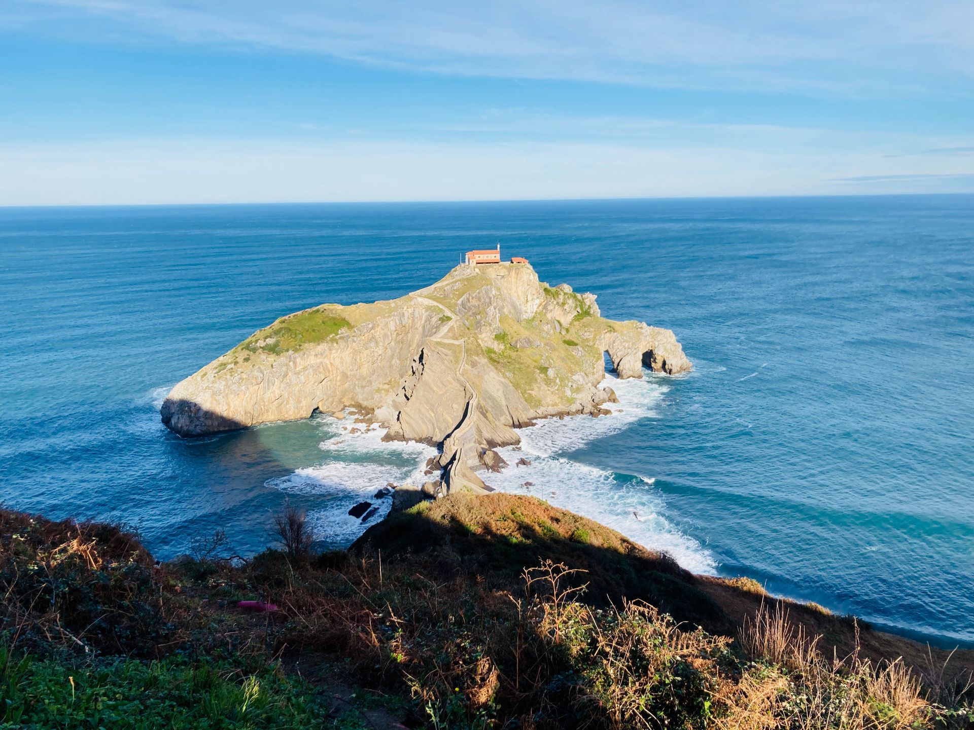 Island with a chapel on top, surrounded by blue ocean, under a clear sky.
