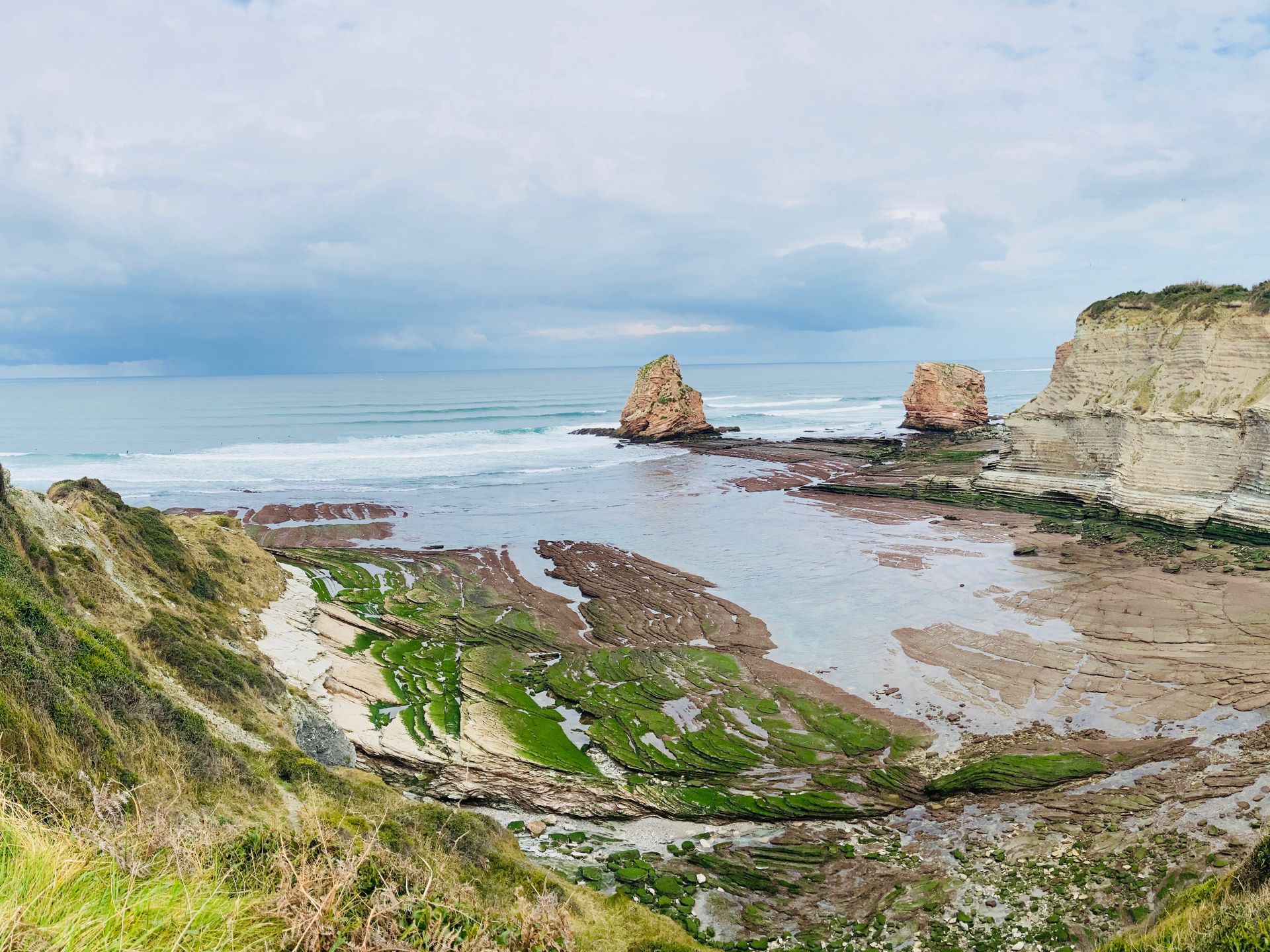 Rocky coastline with cliffs, two large rock formations in the water, and an overcast sky.