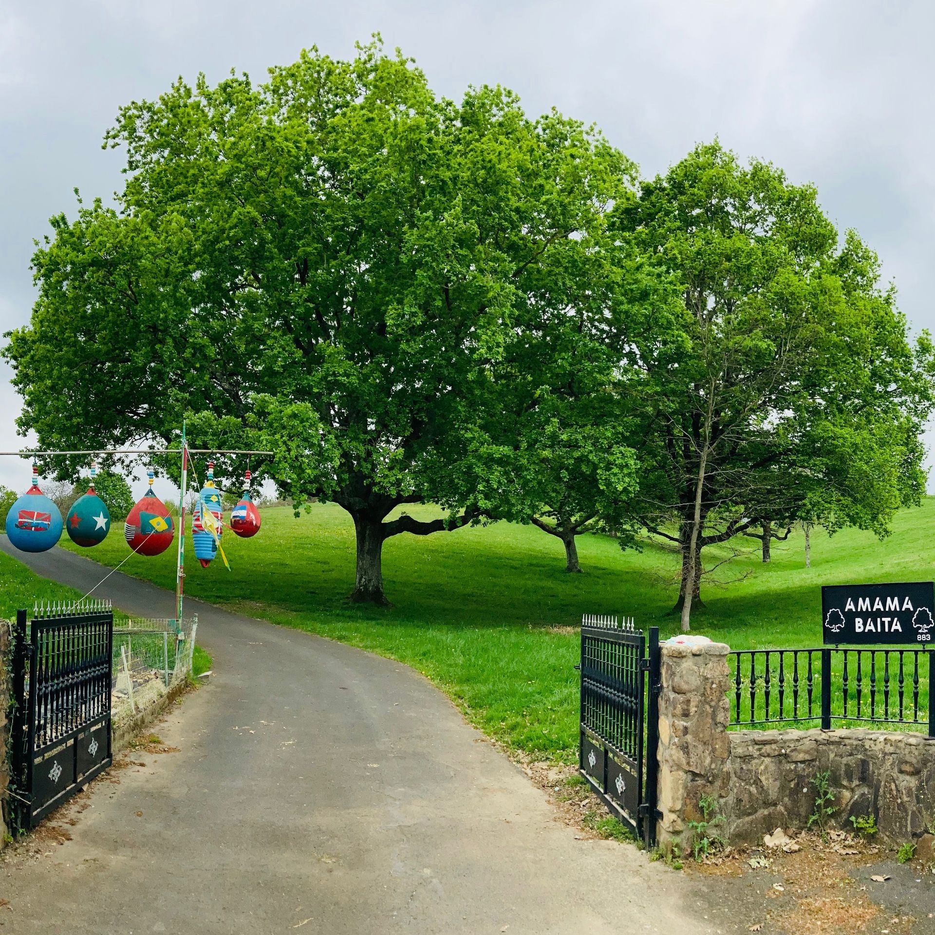 Park entrance with a path, trees, and decorations. Cloudy sky.