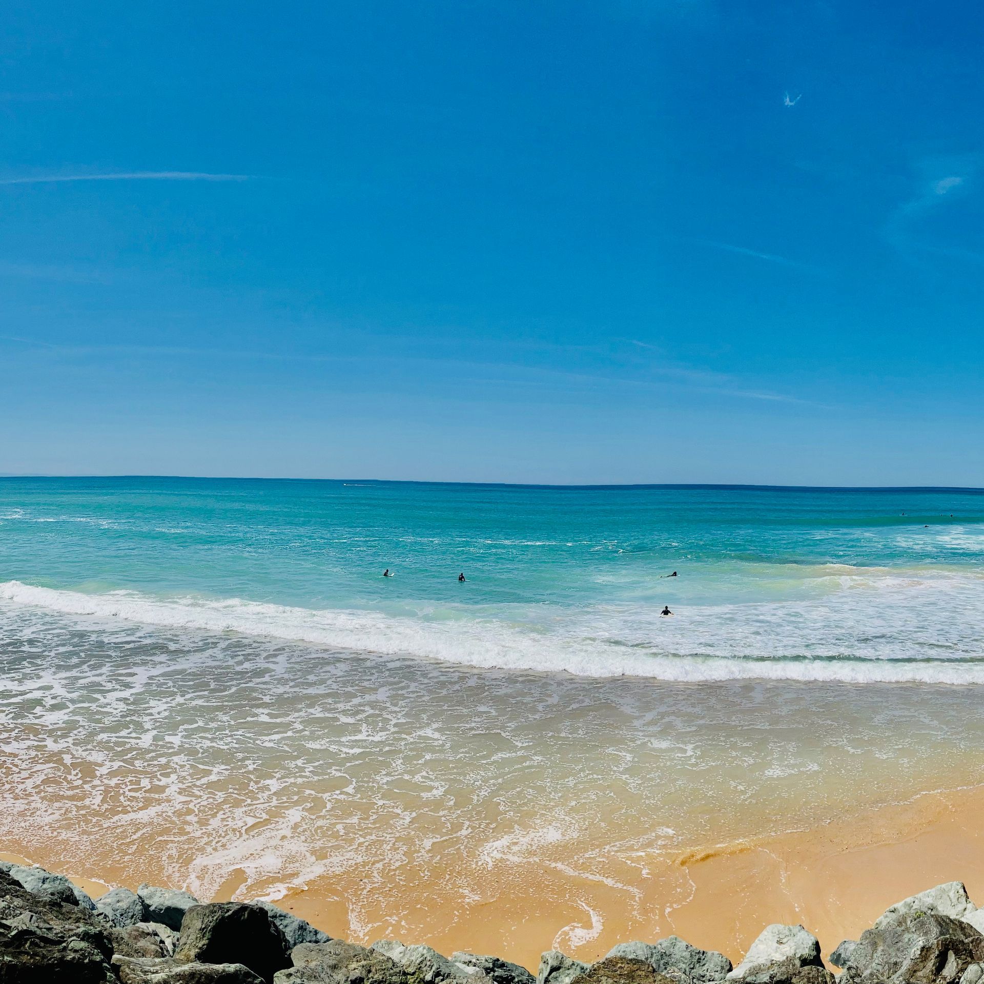 Blue ocean waves washing onto a golden sand beach under a clear blue sky.