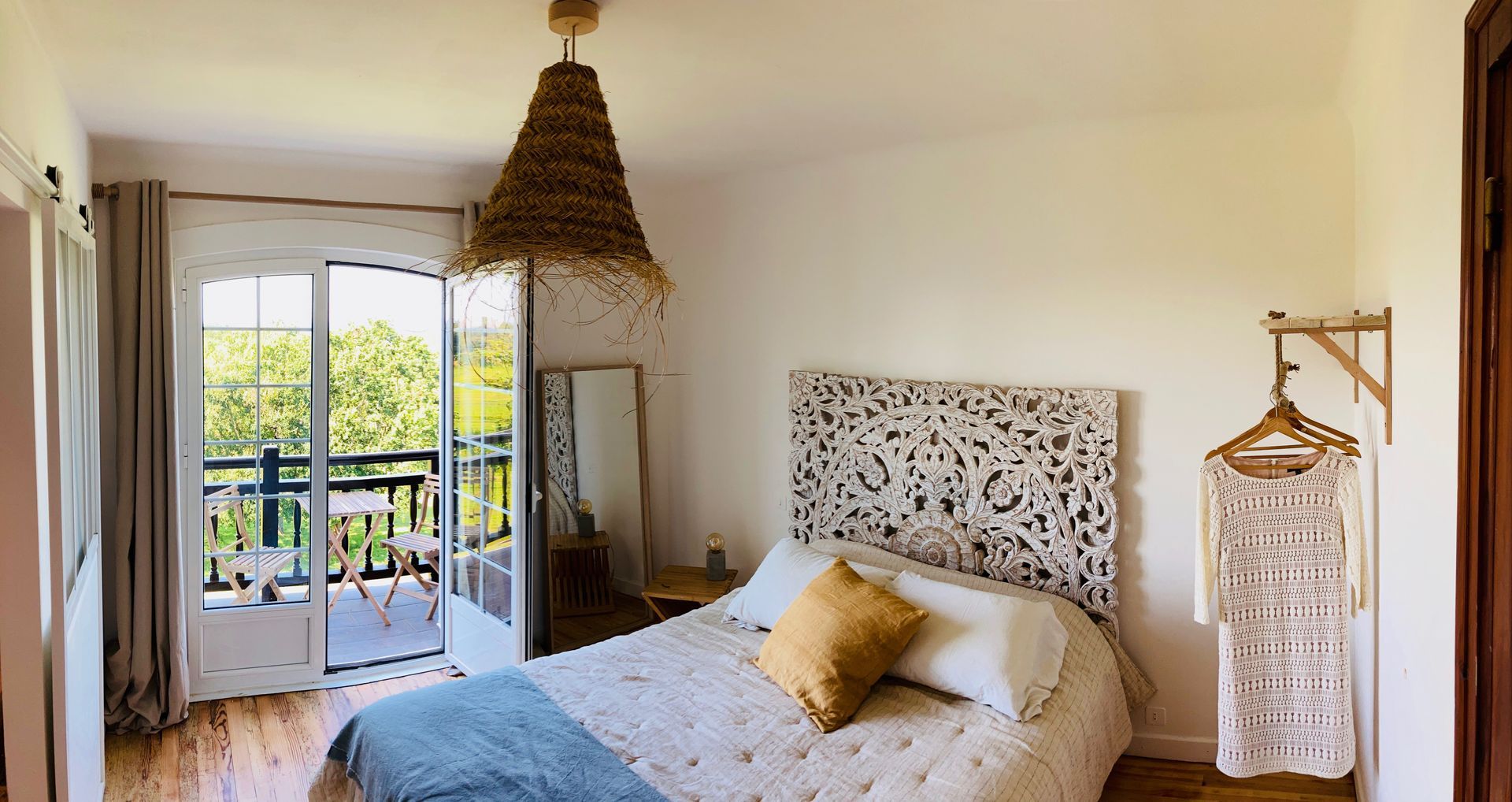 Bedroom with a bed, balcony, and woven lampshade; white walls and wooden floor.
