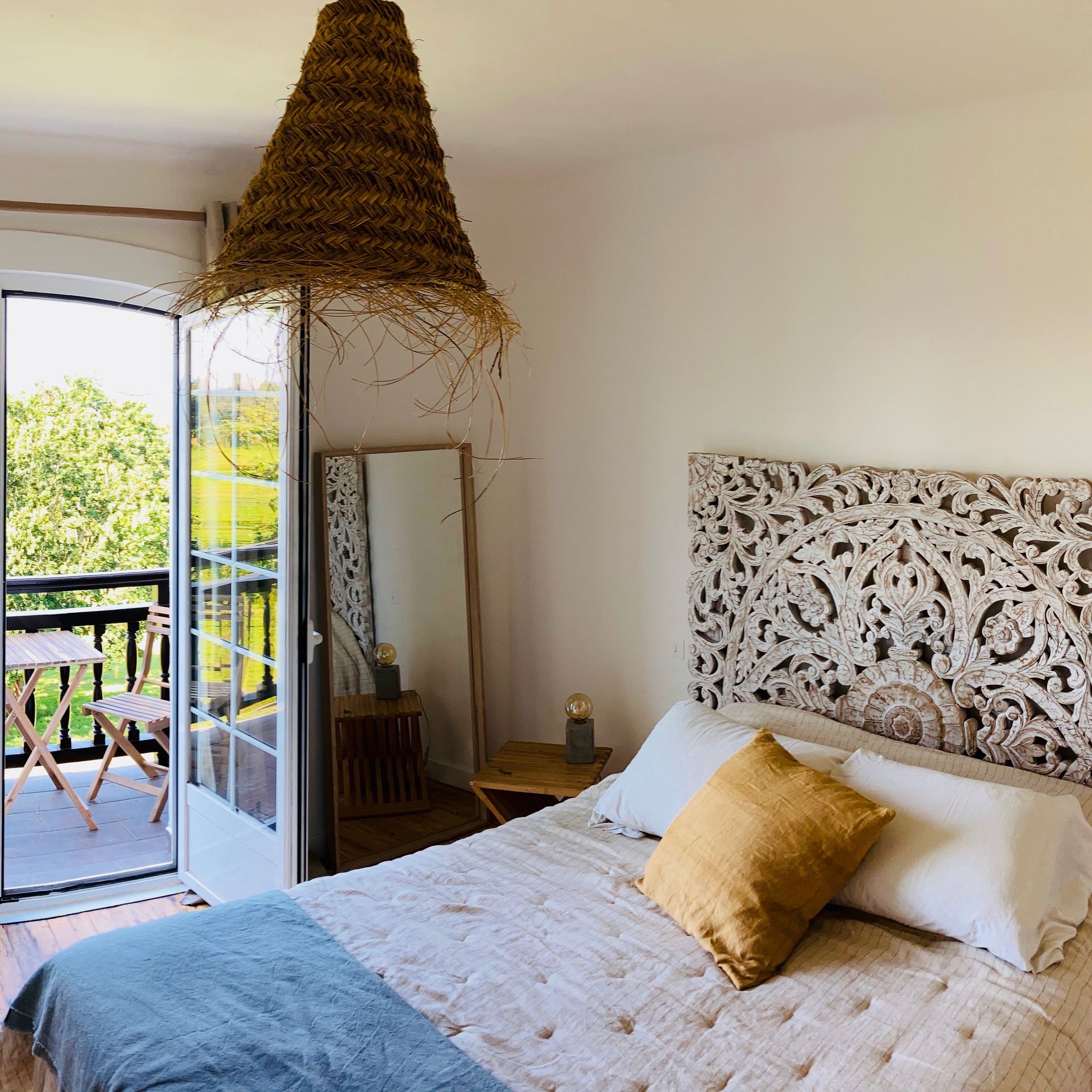 Bedroom with balcony access, featuring bed with carved headboard, straw pendant light, and mirror.