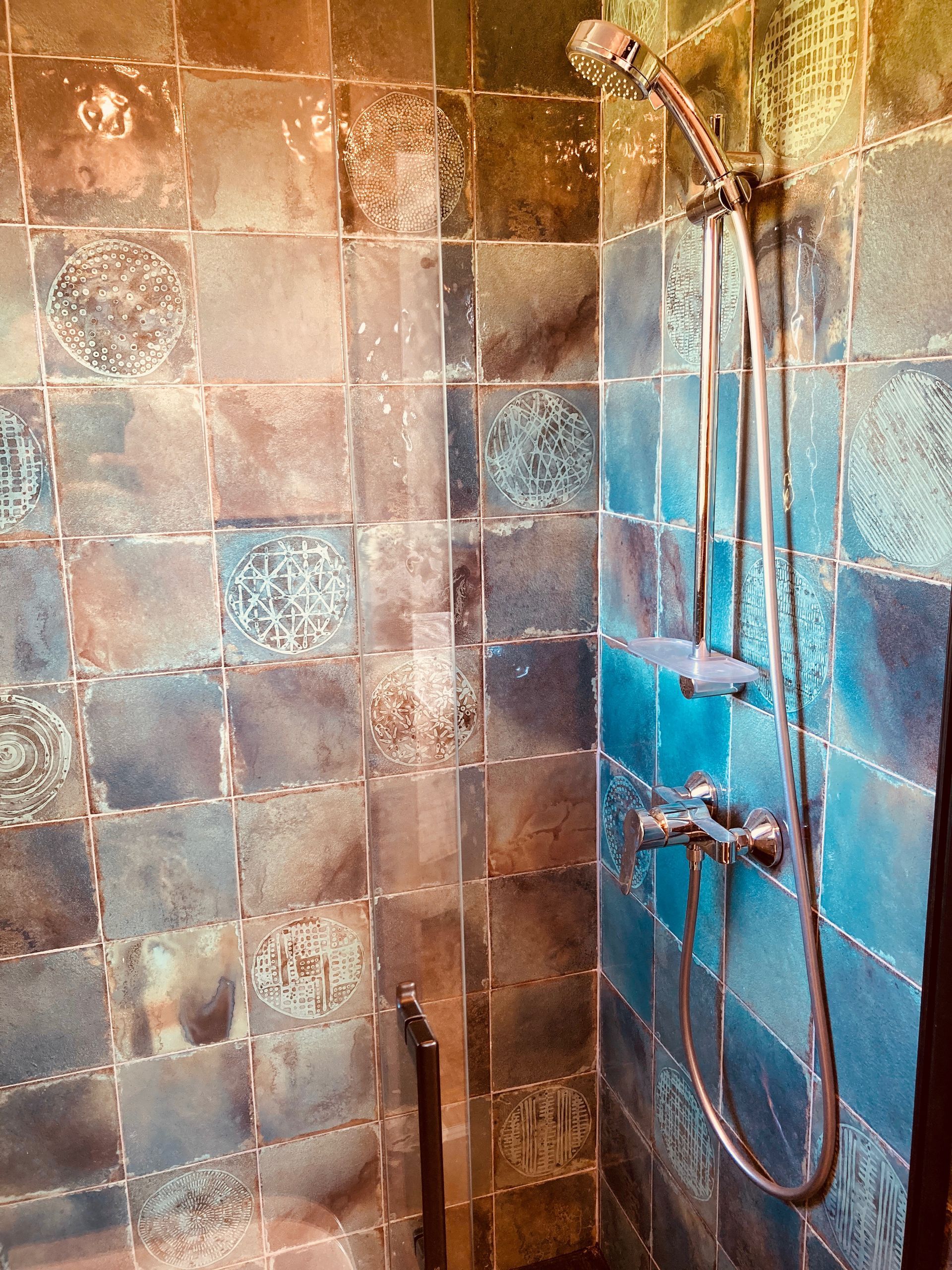 Blue tiled shower with chrome fixtures.