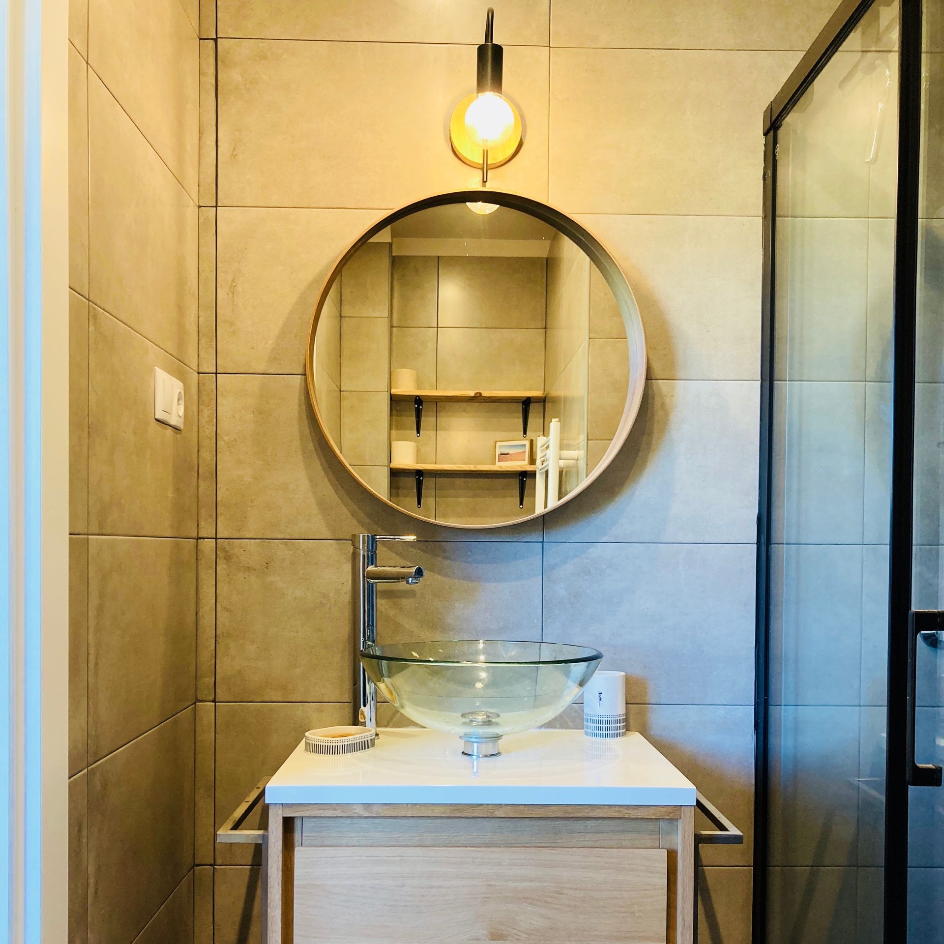 Bathroom with a round mirror, glass sink, and a hanging light.