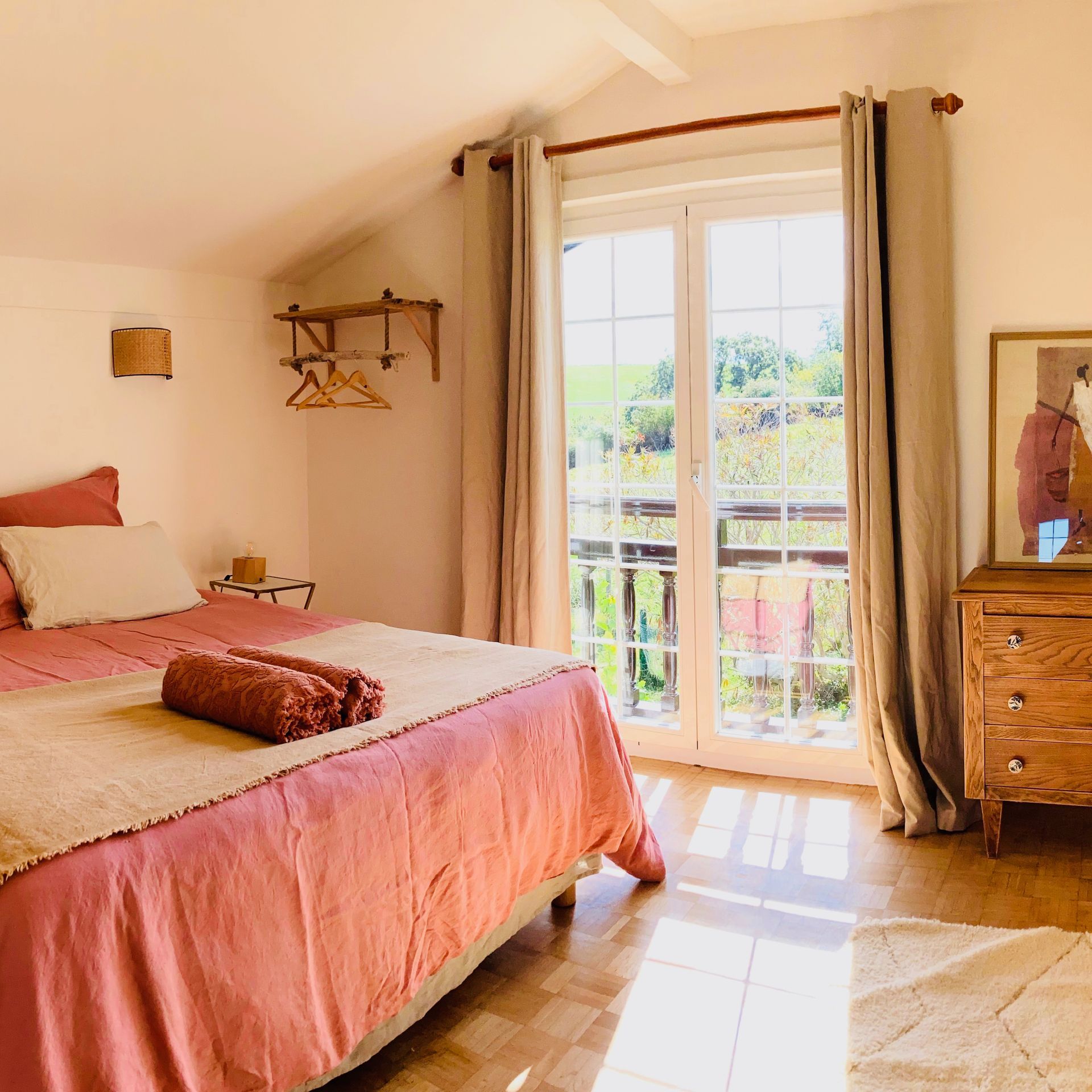 Bedroom with pink bedding, French doors to a balcony, and wooden dresser.