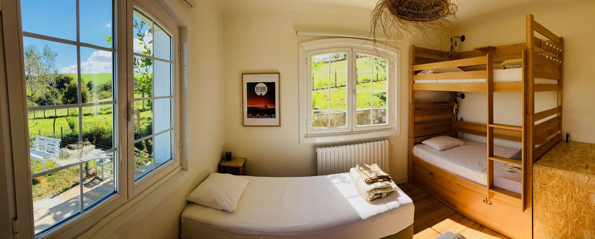 Bedroom with a single bed, bunk beds, and windows overlooking a green landscape.
